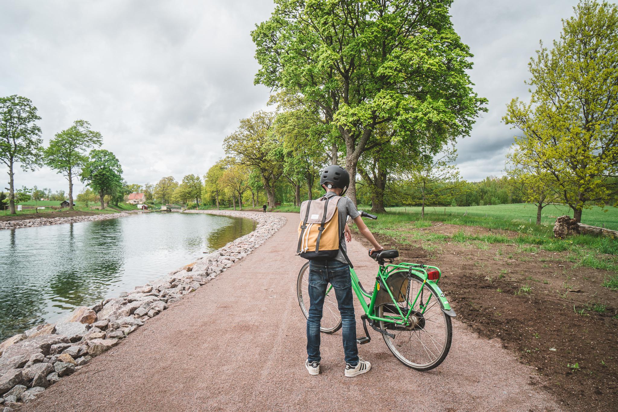 Een jongen staat naast zijn groene fiets op een weg langs het water van het Götakanaal.
