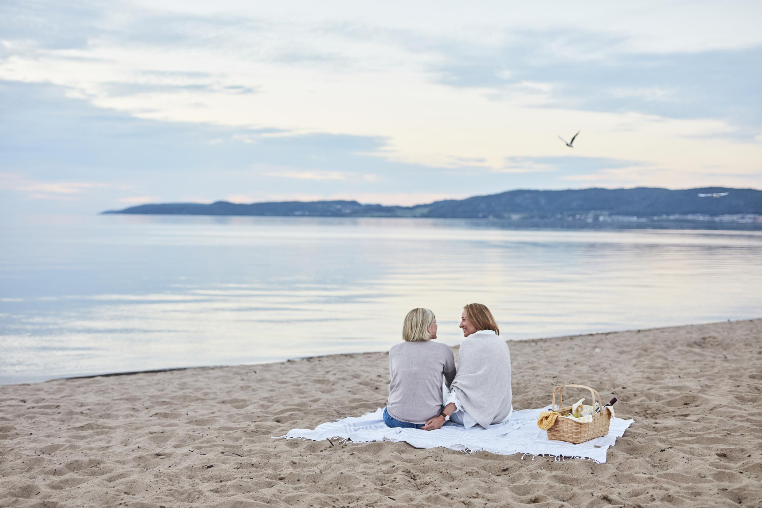Twee vrouwen zitten op een deken op een strand.