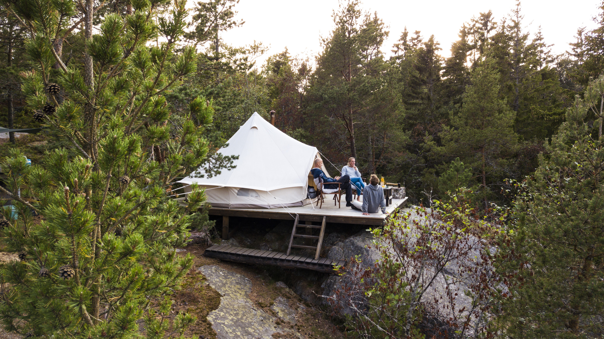 Three people sits outside a glamping tent.