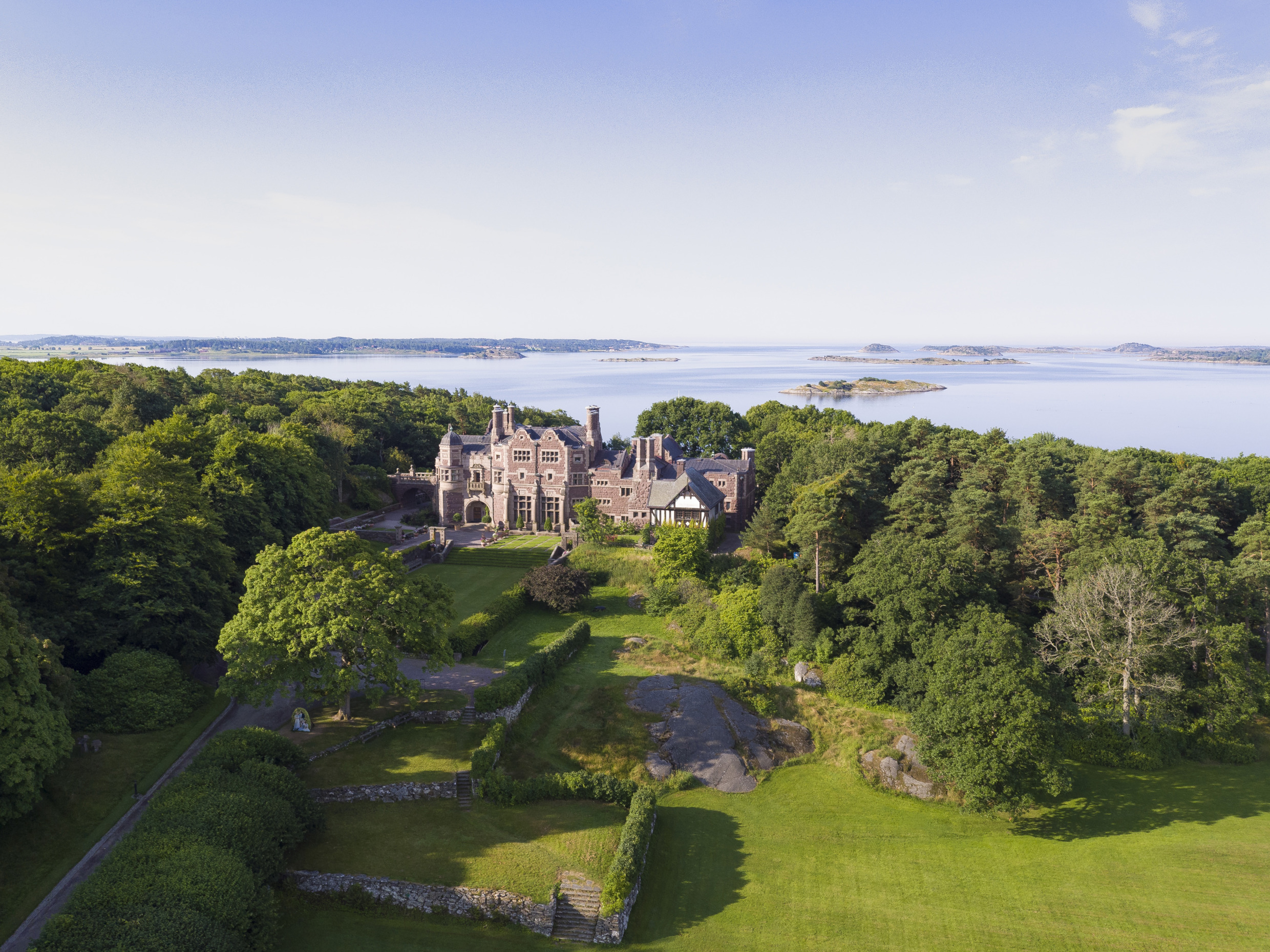 Een luchtfoto van kasteel Tjolöholm naast het water en omgeven door groen in de zomer.