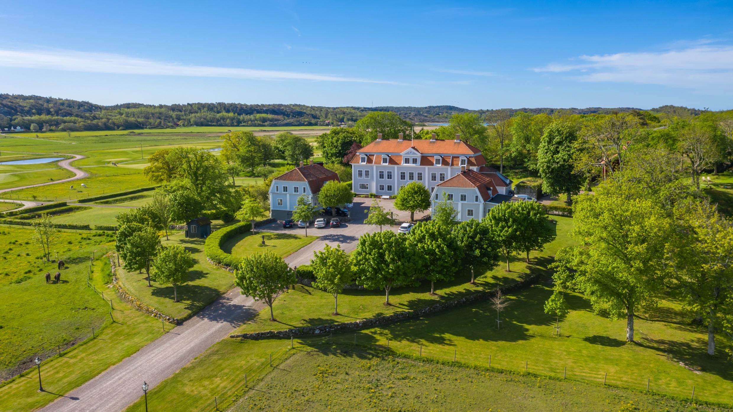Luchtfoto van een herenhuis bestaande uit drie grote houten gebouwen. Een haag, bomen en groen omringen het landhuis.