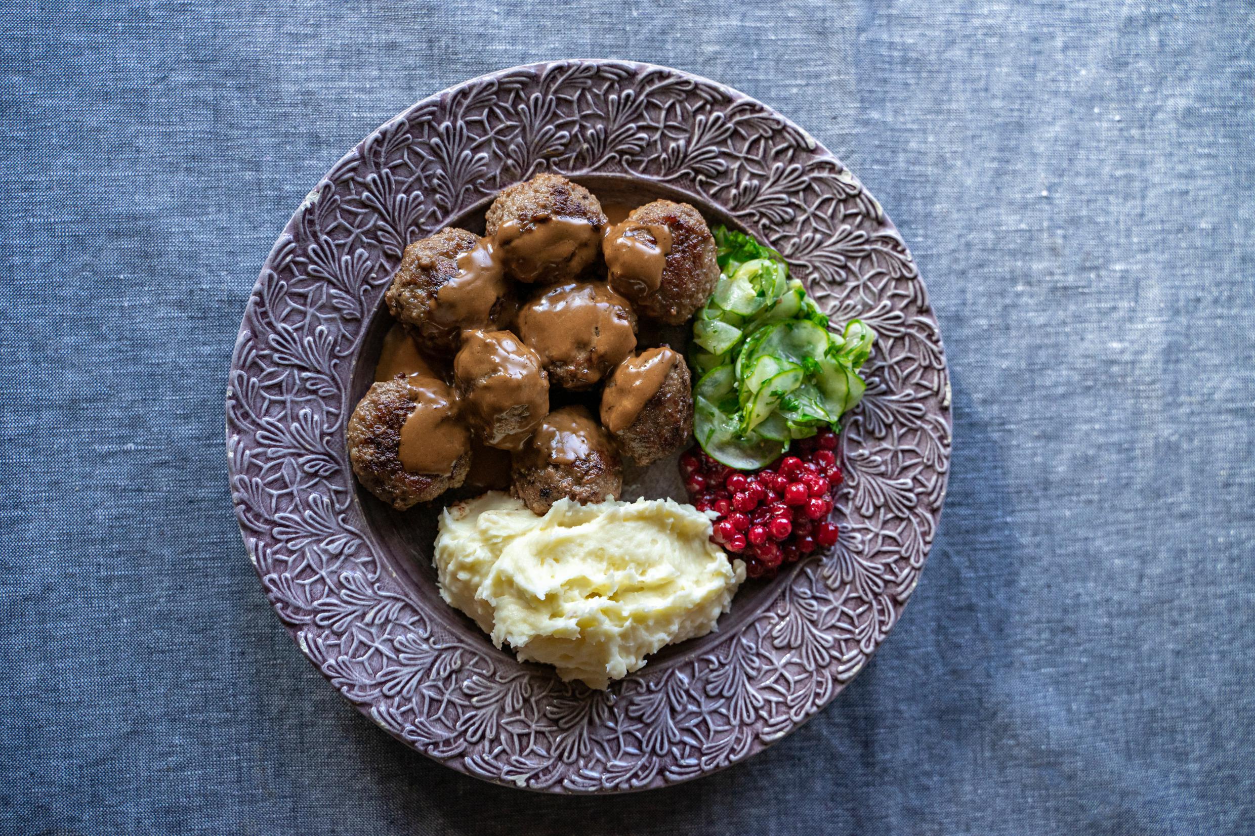 Une assiette avec des boulettes de viande, de la purée de pommes de terre, des airelles et du concombre mariné.