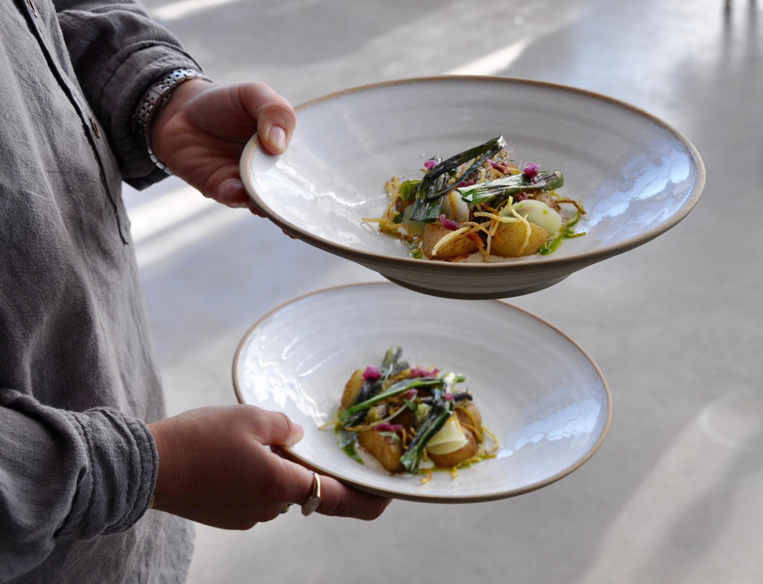 You see part of a person holding two plates with a colorful vegetarian dish at a restaurant.