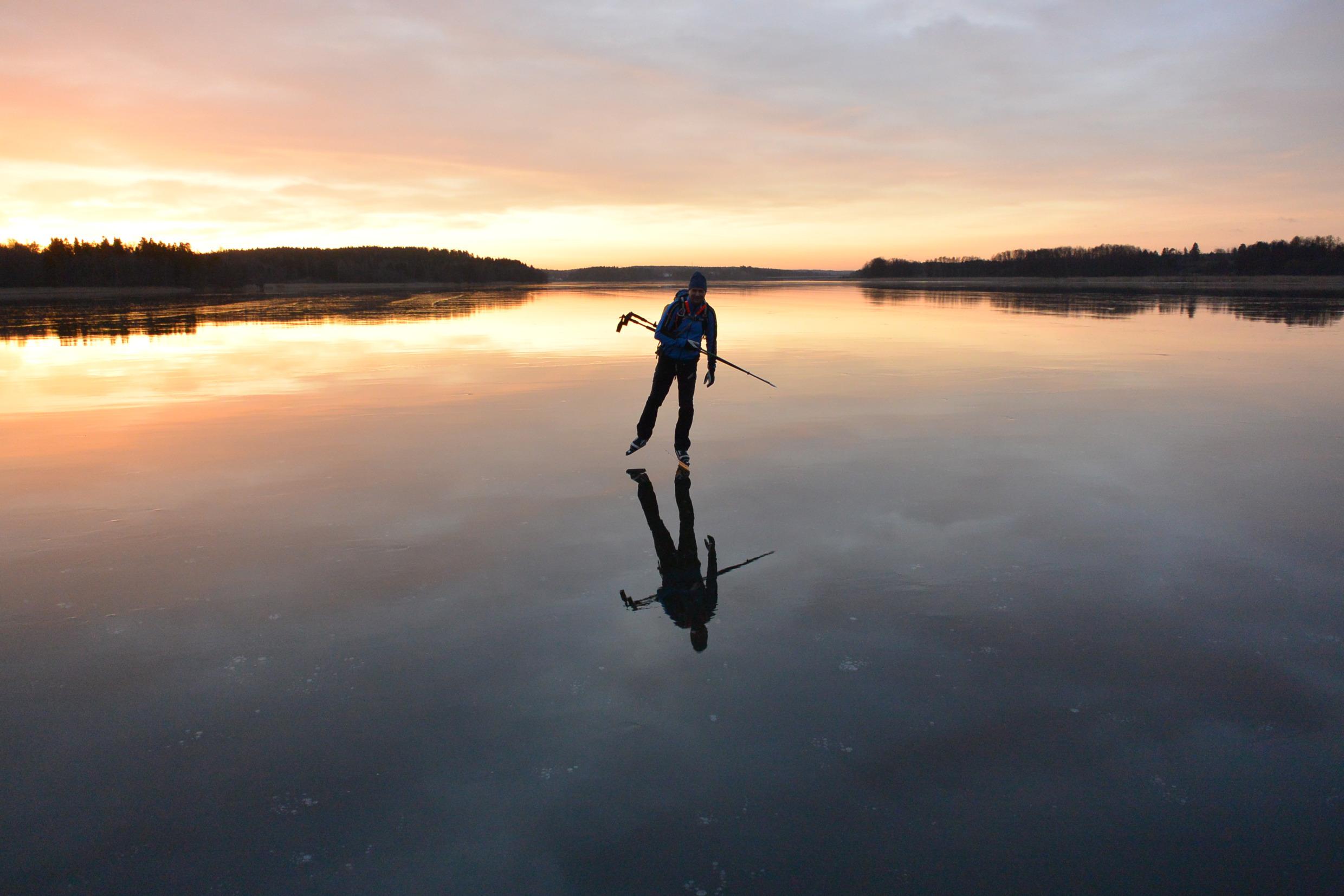 A person ice skating on a frozen lake at dusk.