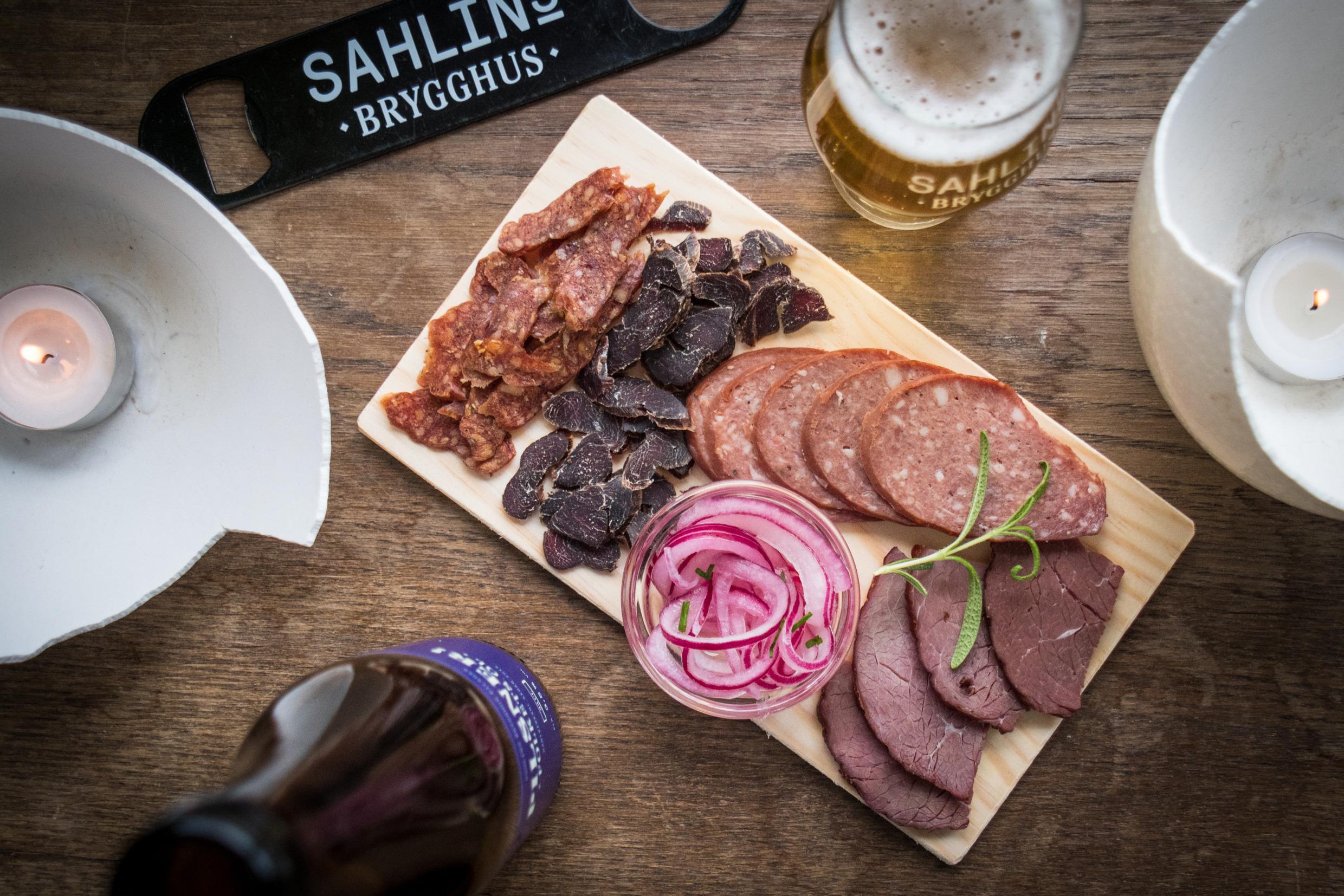 Verschillende soorten worst geserveerd op een houten dienblad, bij een flesje bier.