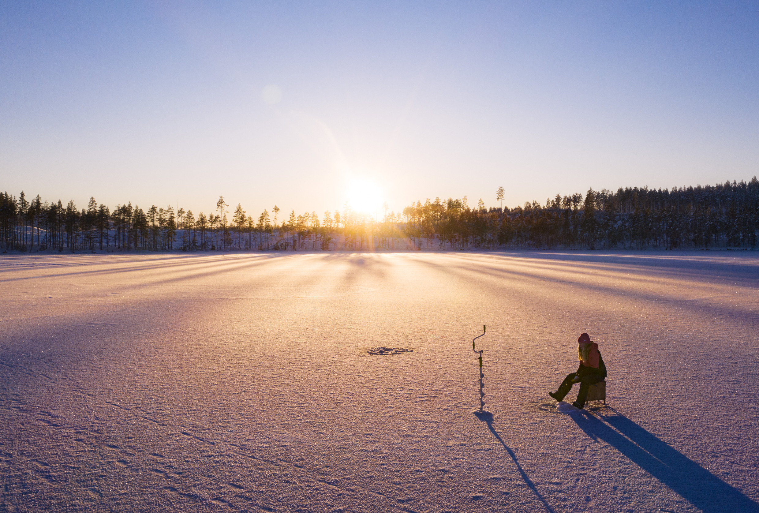 Une femme pêchant au trou par une belle journée d'hiver.