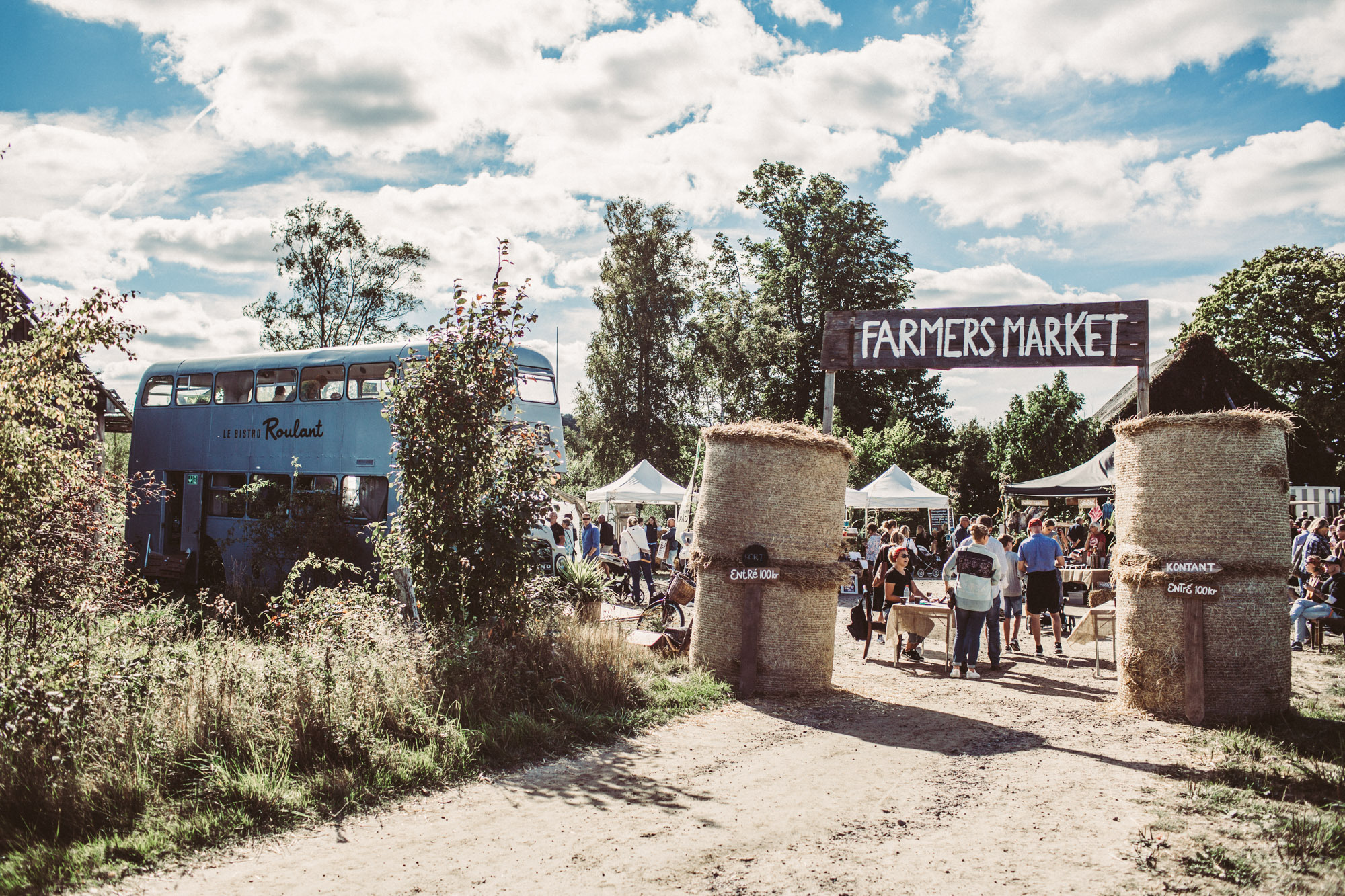 Ein großes Schild mit der Aufschrift "Farmers Market" (Bauernmarkt) ist am Eingang eines ländlichen Marktes zu sehen. Ein hellblauer Bus ist an der Seite geparkt.