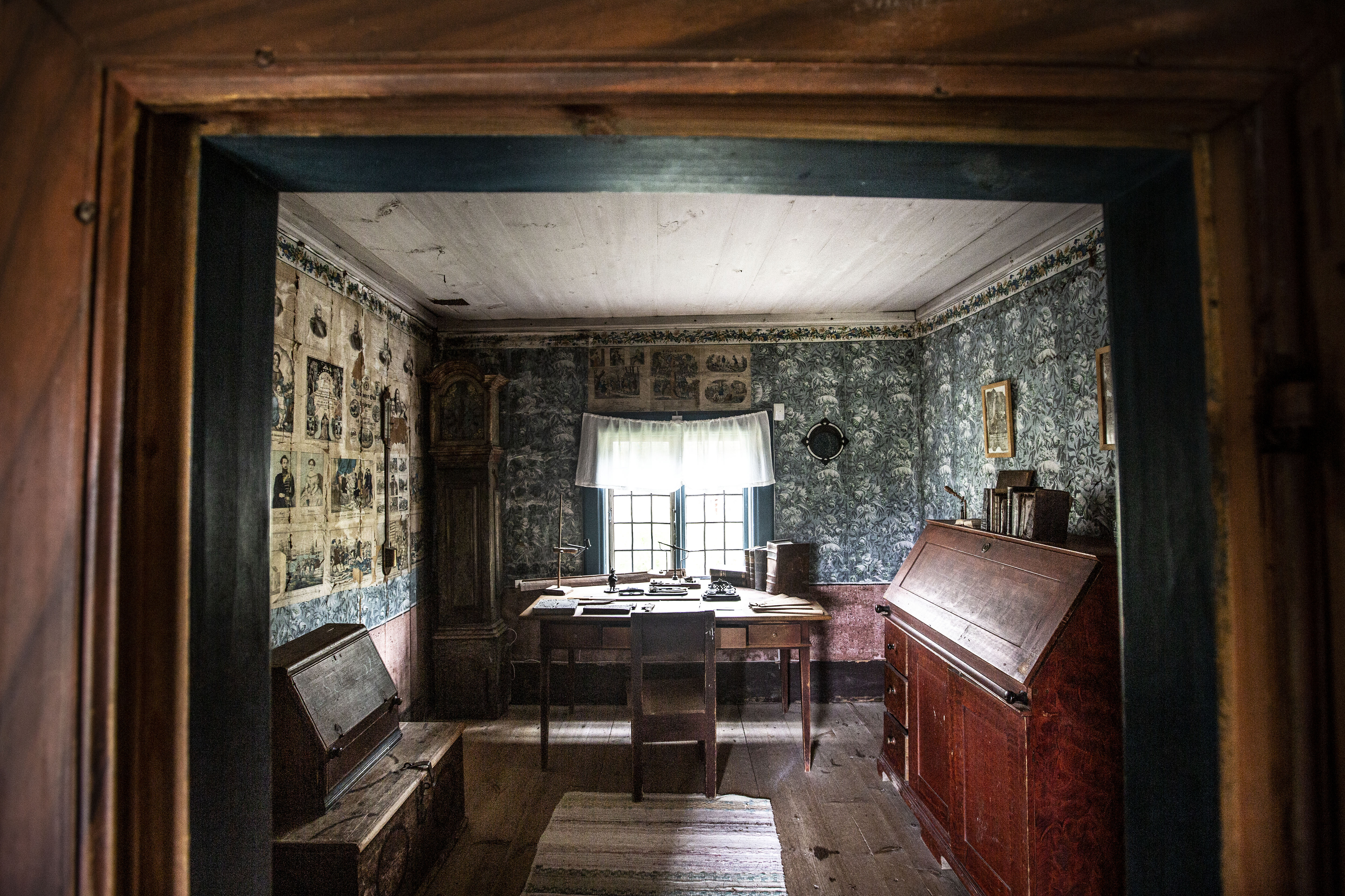 Historic study room at Fågelsjö Gammelgård with wooden furniture, wall art and patterned wallpaper.