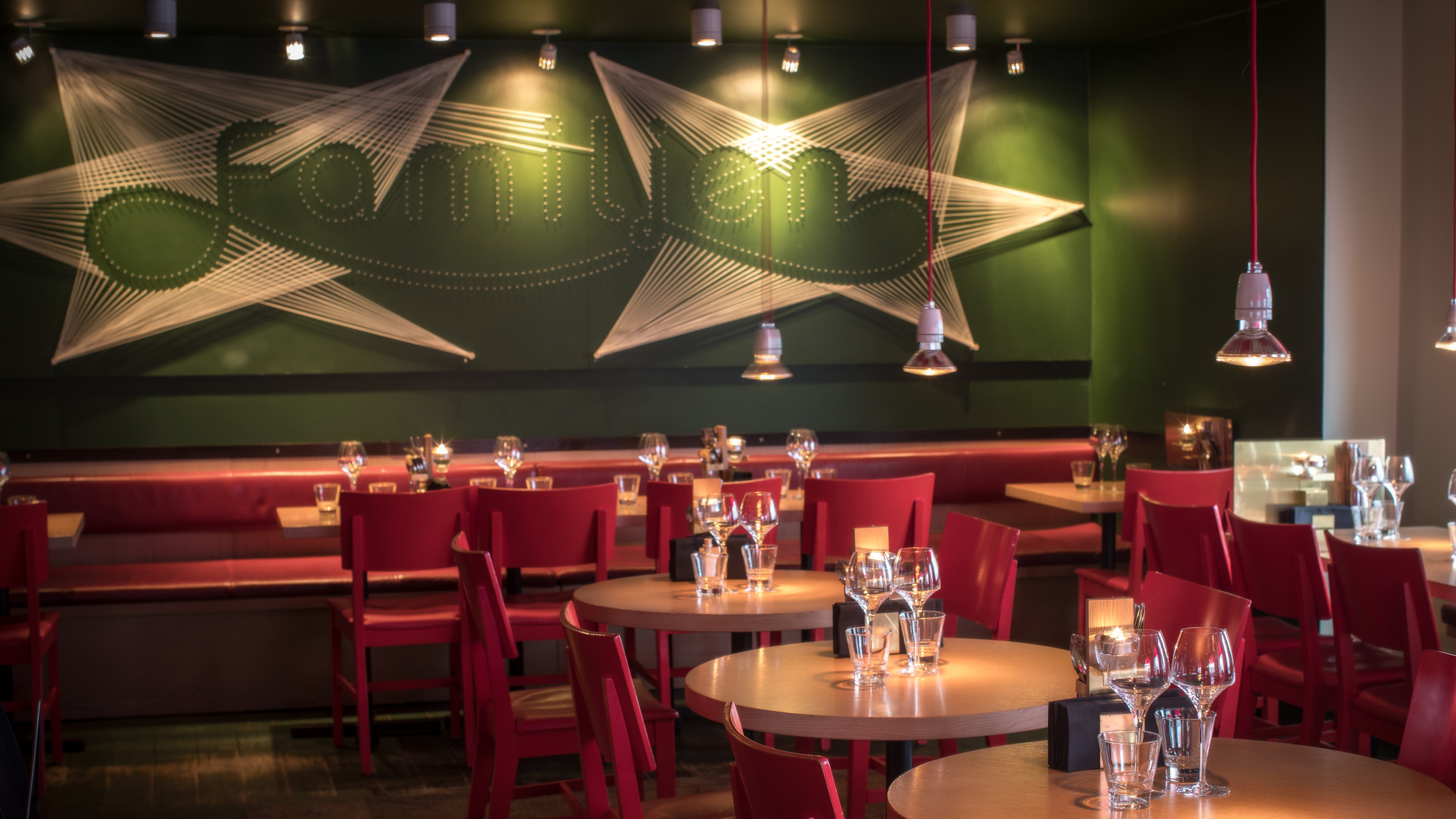 L'intérieur du restaurant Familjen à Göteborg, avec des chaises rouges, des tables en bois avec des verres à vin, et un mur vert avec des cordes décoratives.