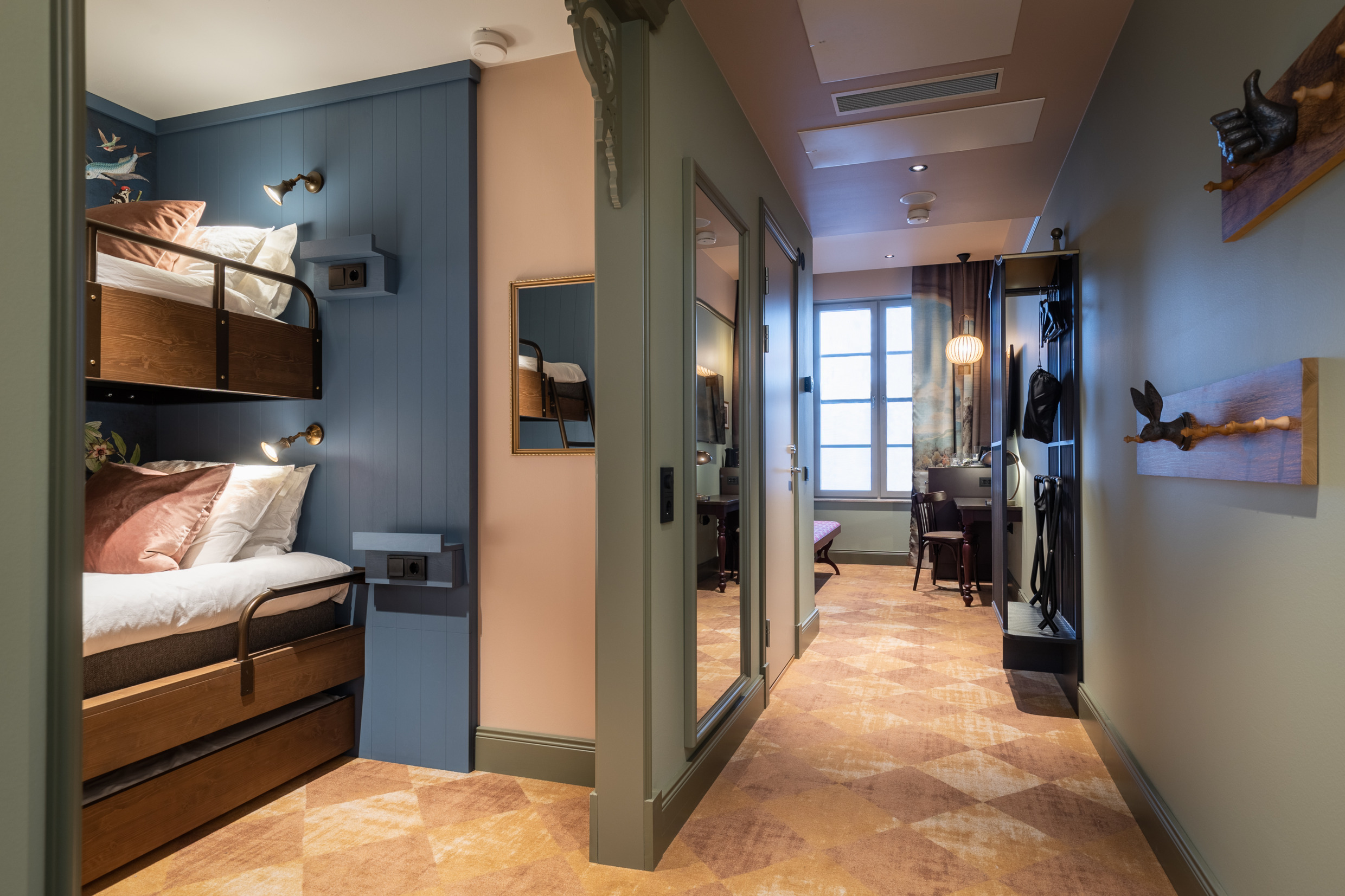 Familiekamer in het Liseberg Grand Curiosa Hotel met een stapelbed voor kinderen, een zichtbare spiegel en kleerhangers in de vorm van een konijnenkop en een hand die een duim omhoog steekt.