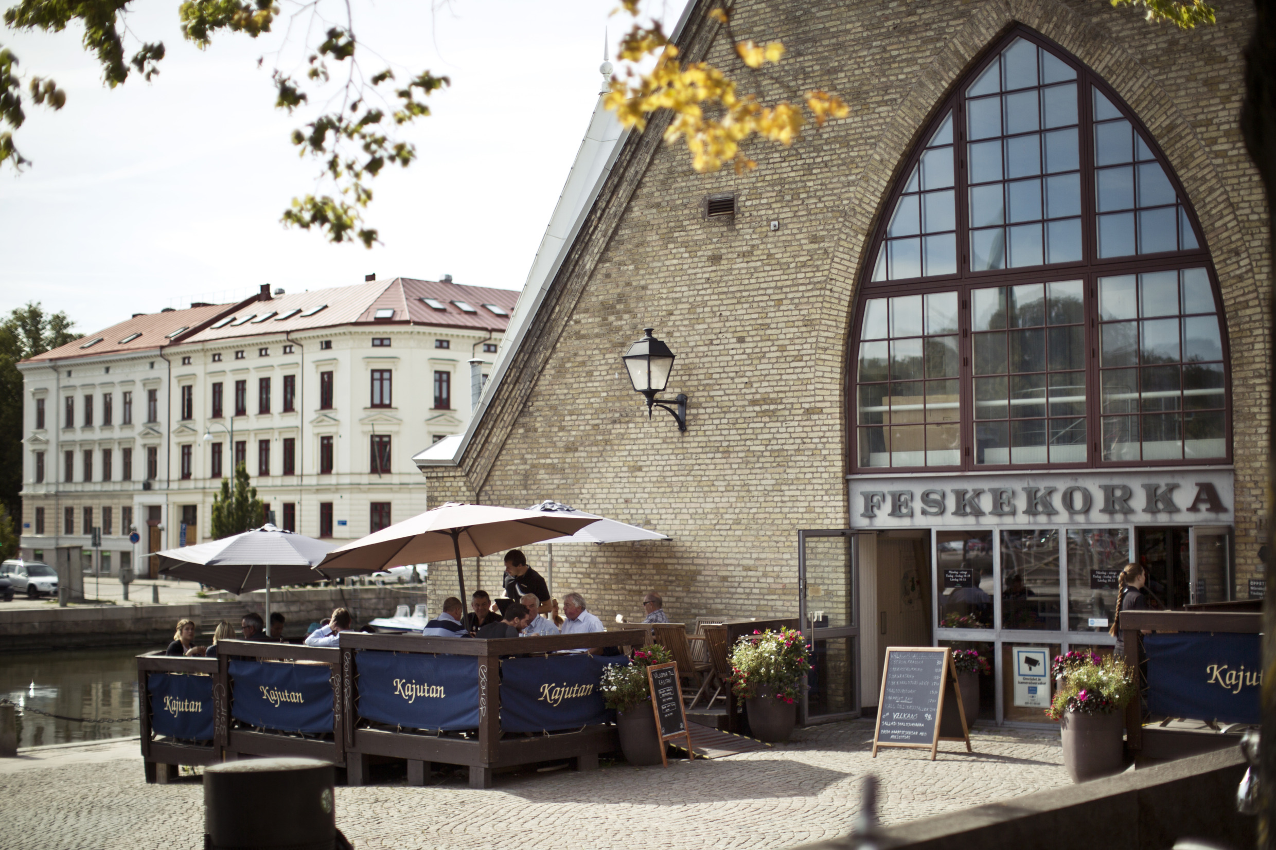 Die Außenansicht der Feskekörka, mit einem großen Glasfenster über dem Eingang. Einige Leute sitzen auf der Terrasse vor dem Gebäude.