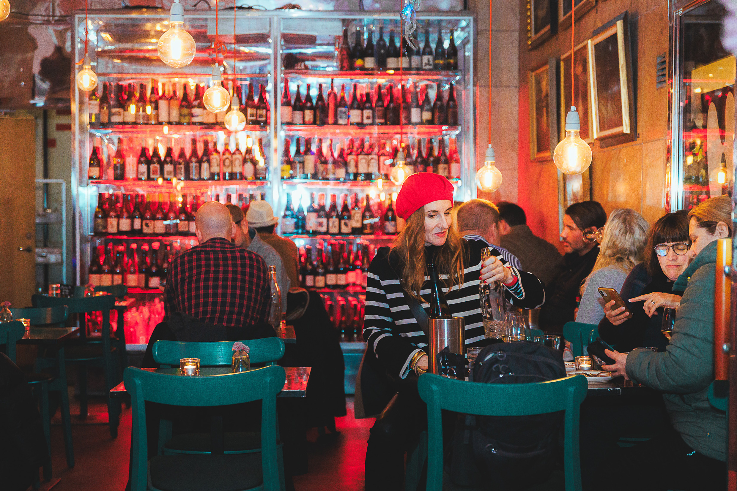 À l'intérieur du bar à vin Folk à Göteborg, les clients prennent un verre dans un cadre agréable, entourés d'un éclairage tamisé, de chaises sarcelles et d'un mur de bouteilles de vin.