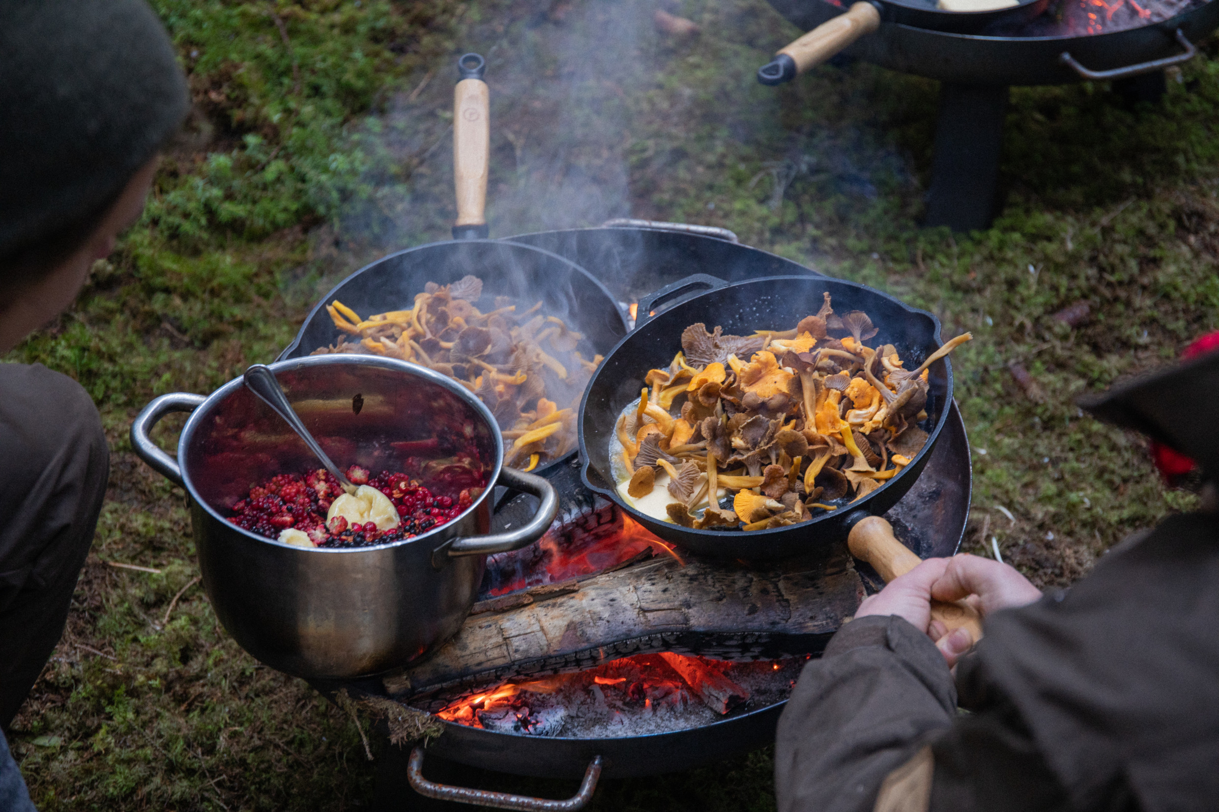 People frying chanterelle and boiling berries outdoors.