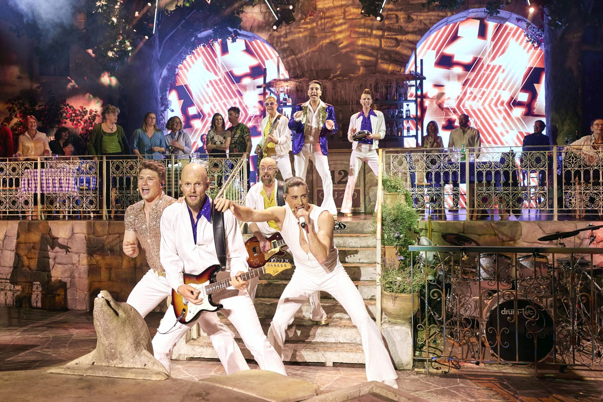 Musiker in weißer Kleidung singen, tanzen und spielen Gitarre auf der Bühne, bei der Mamma Mia!The Party Veranstaltung in Stockholm