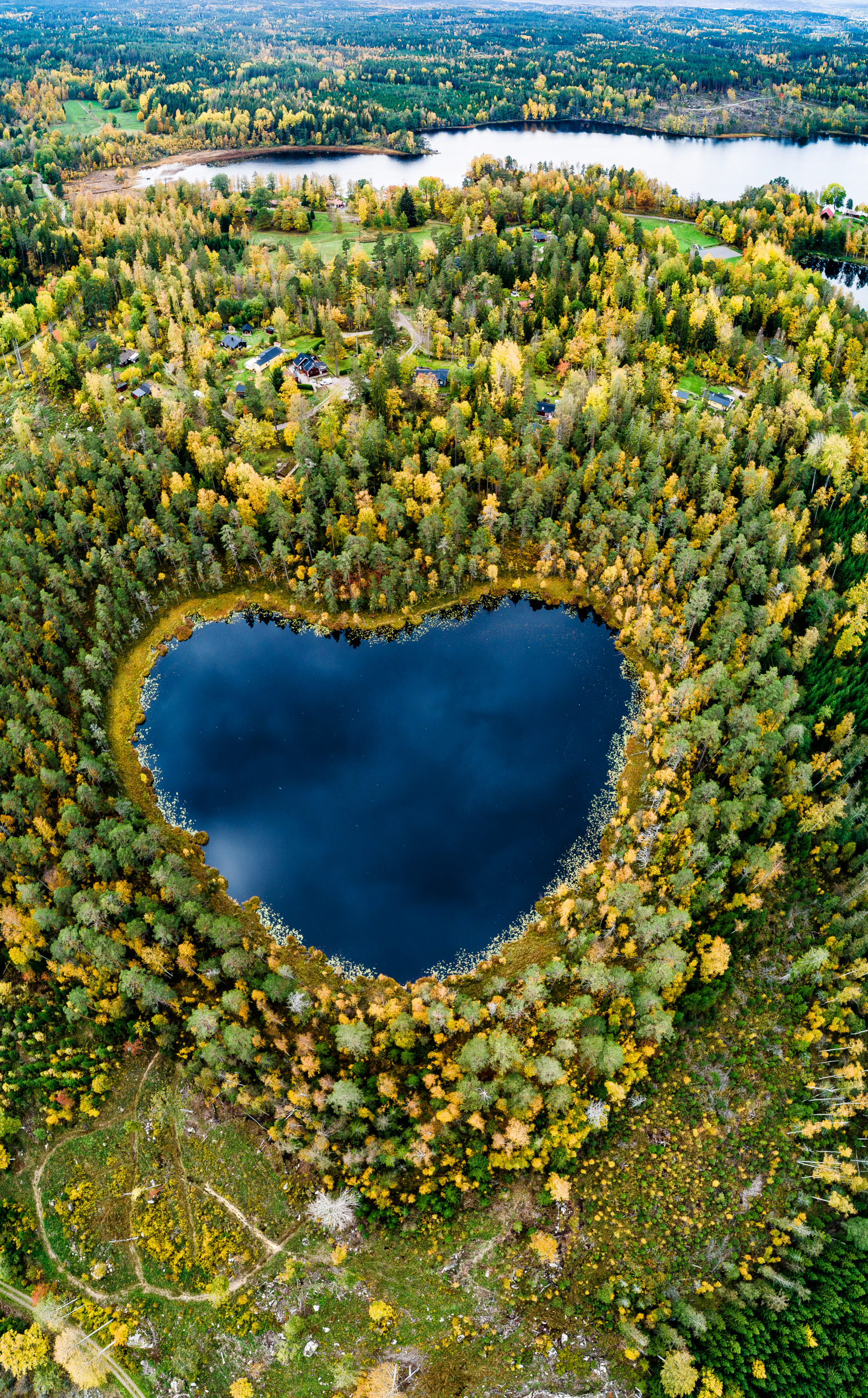 Een dronefoto van een hartvormig meer. Rondom het meer staan bomen in herfstkleuren.