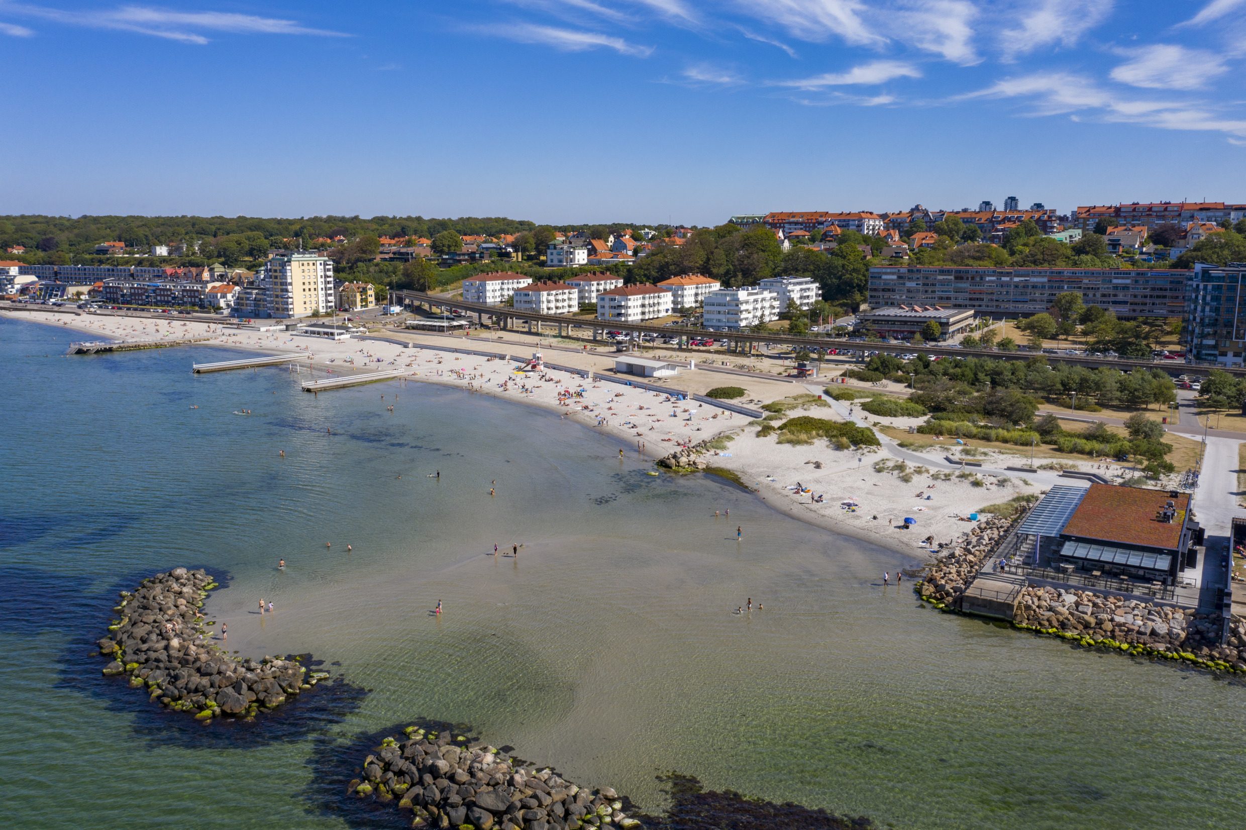 Luftaufnahme des Strandes Fria Bad in Helsingborg mit Schwimmern, weißem Sand und Stadtbild im Hintergrund.