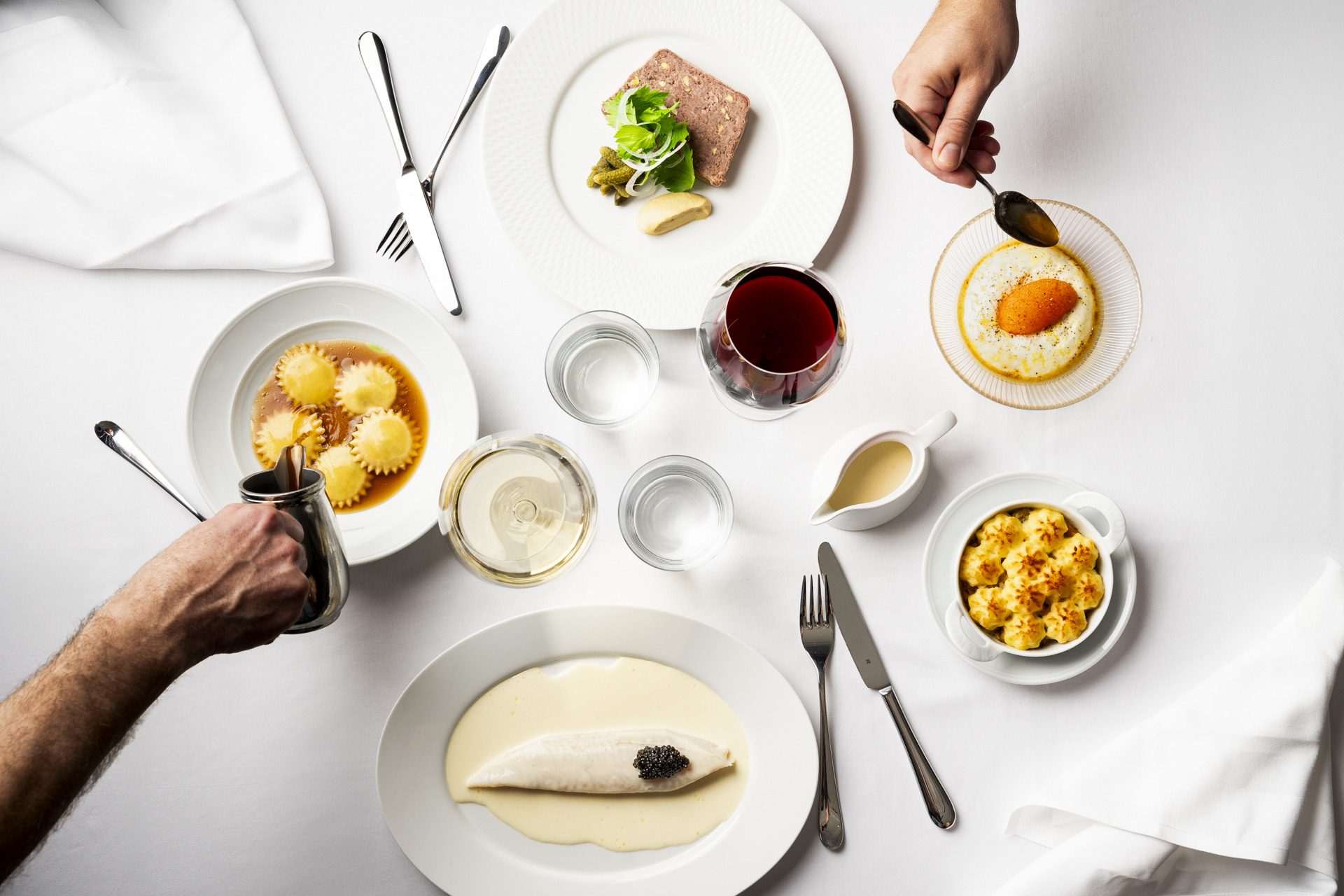 Een gedekte tafel bij restaurant Gondolen met diverse gerechten en drankjes in glazen, door handen geserveerd.