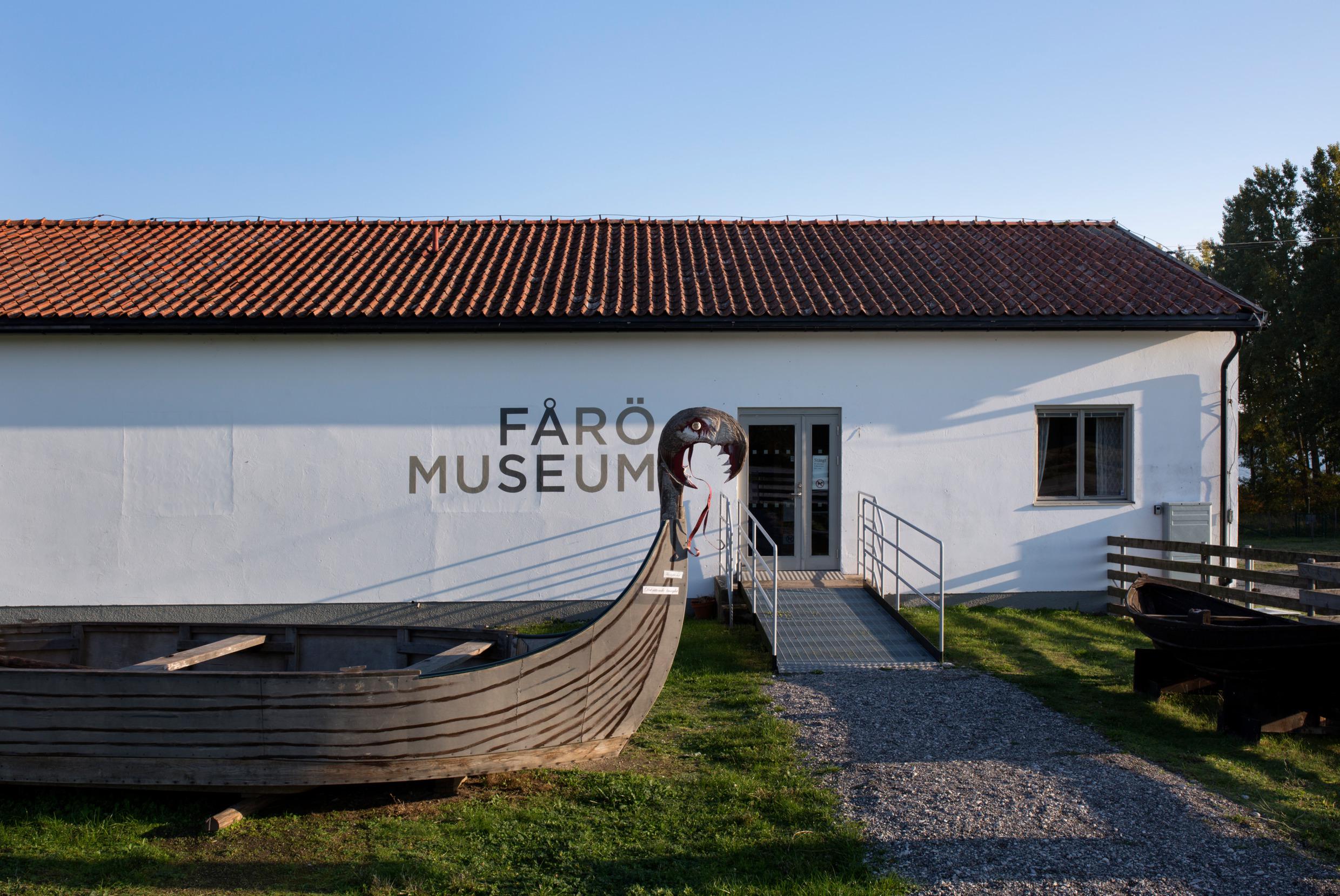 Ein hölzernes Wikingerschiff liegt auf dem Rasen vor einem Haus, auf dem Fårö Museum steht.