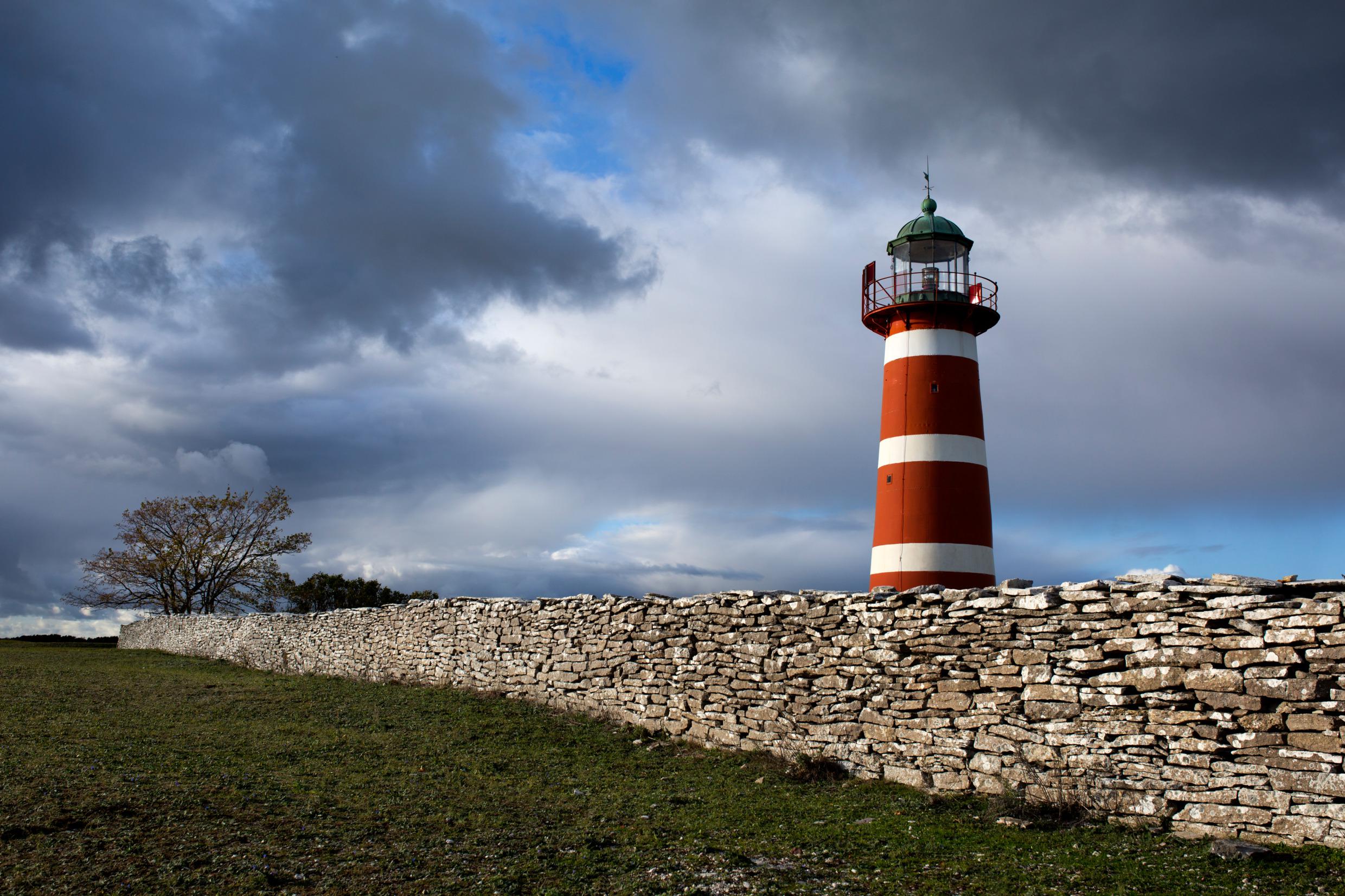 Achter een stenen muur staat een vuurtoren. De lucht is bewolkt.