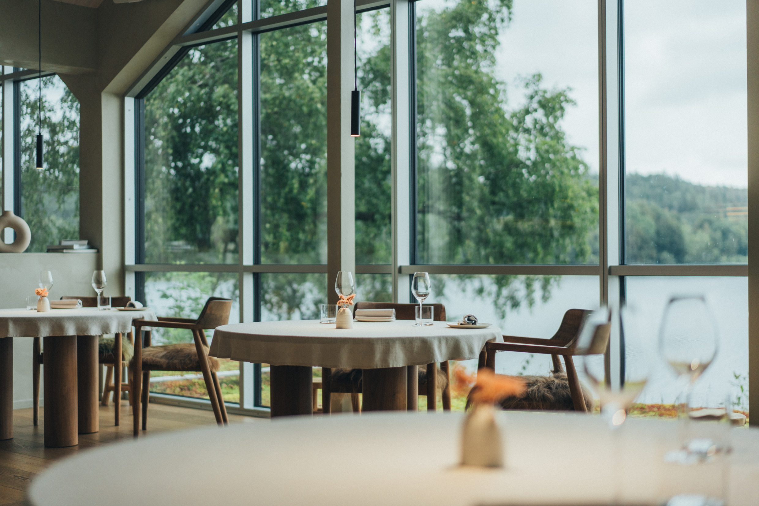 L'intérieur du restaurant Signum, où les tables sont élégamment dressées avec des nappes blanches, de grandes fenêtres et une vue pittoresque sur un lac et une végétation luxuriante.