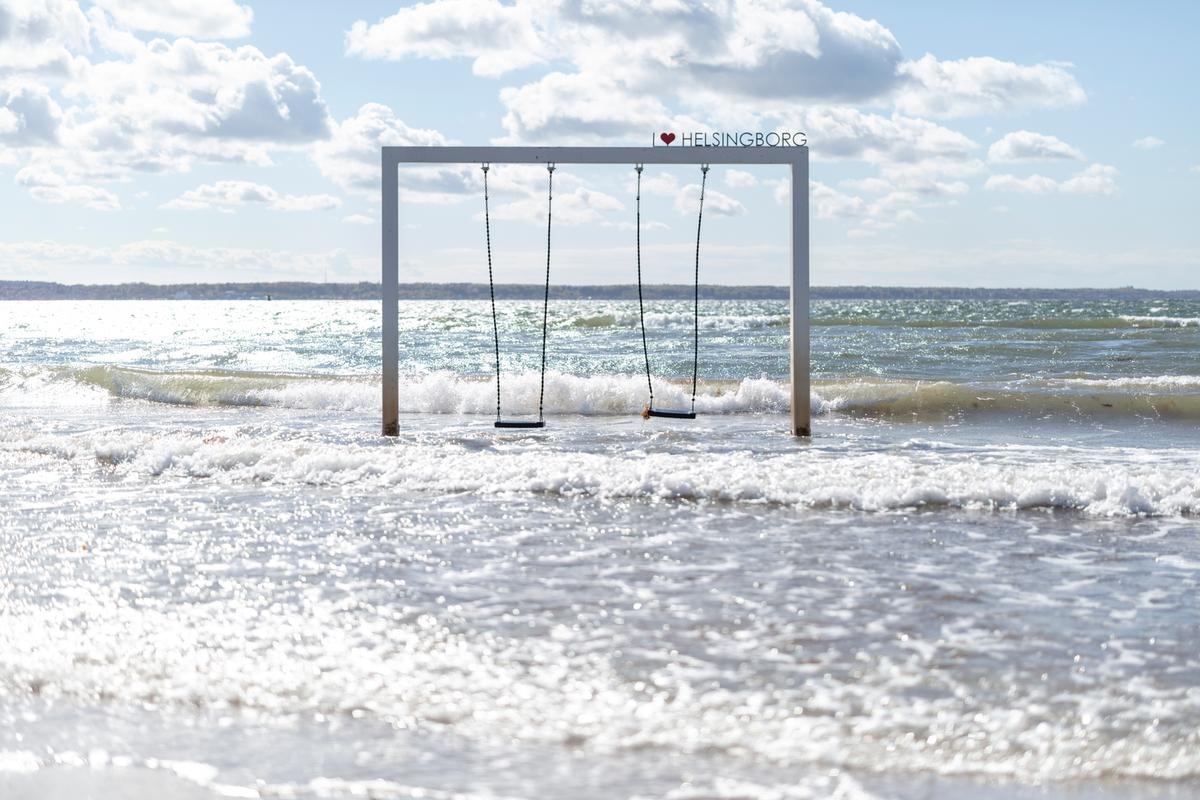 Schaukeln im Meer am Fria Bad Strand in Helsingborg, mit Wellen, die unter einem Rahmen mit der Aufschrift „I Herz Helsingborg“ brechen.