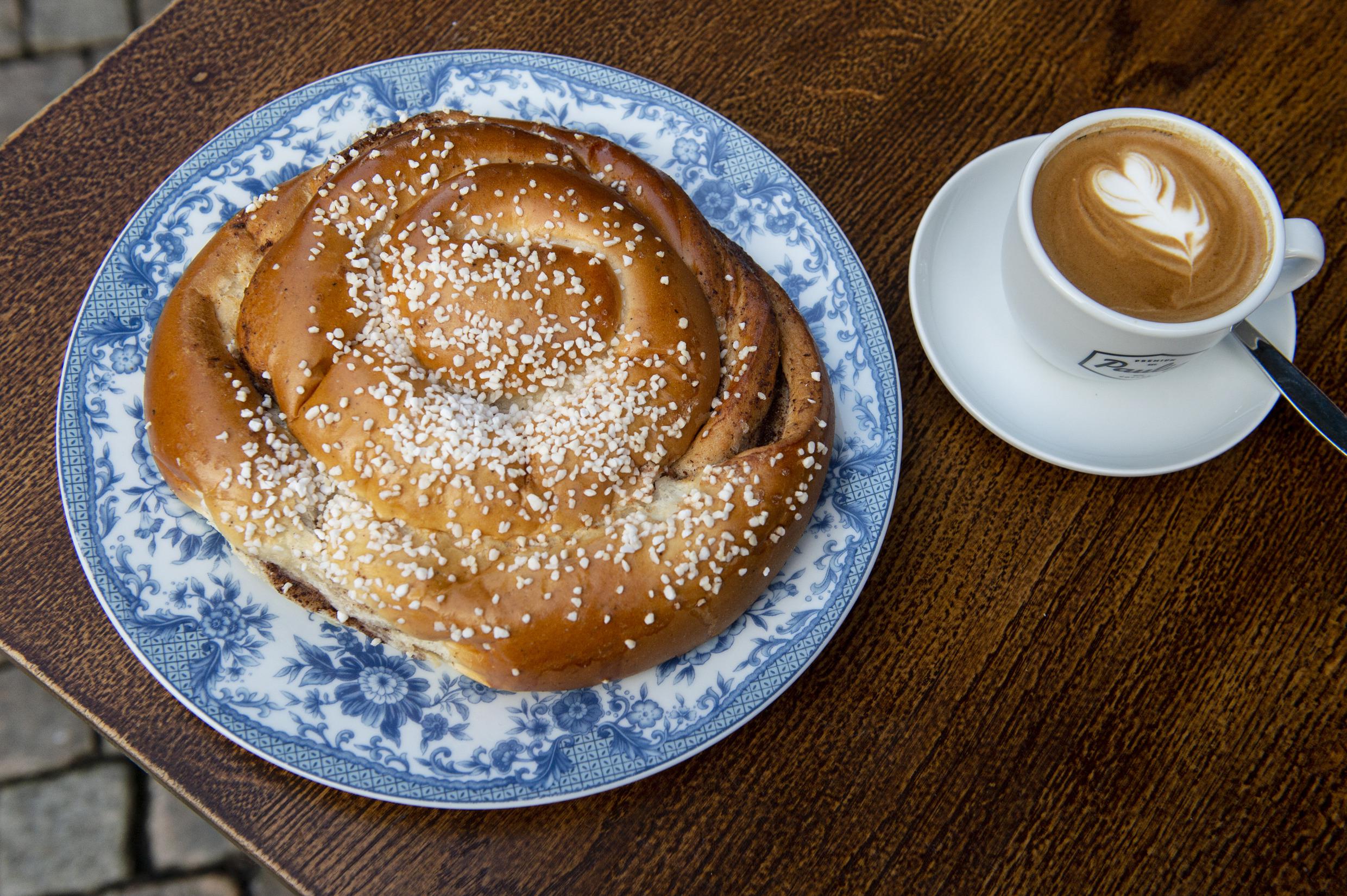 Een enorm kaneelbroodje naast een kopje cappuccino.