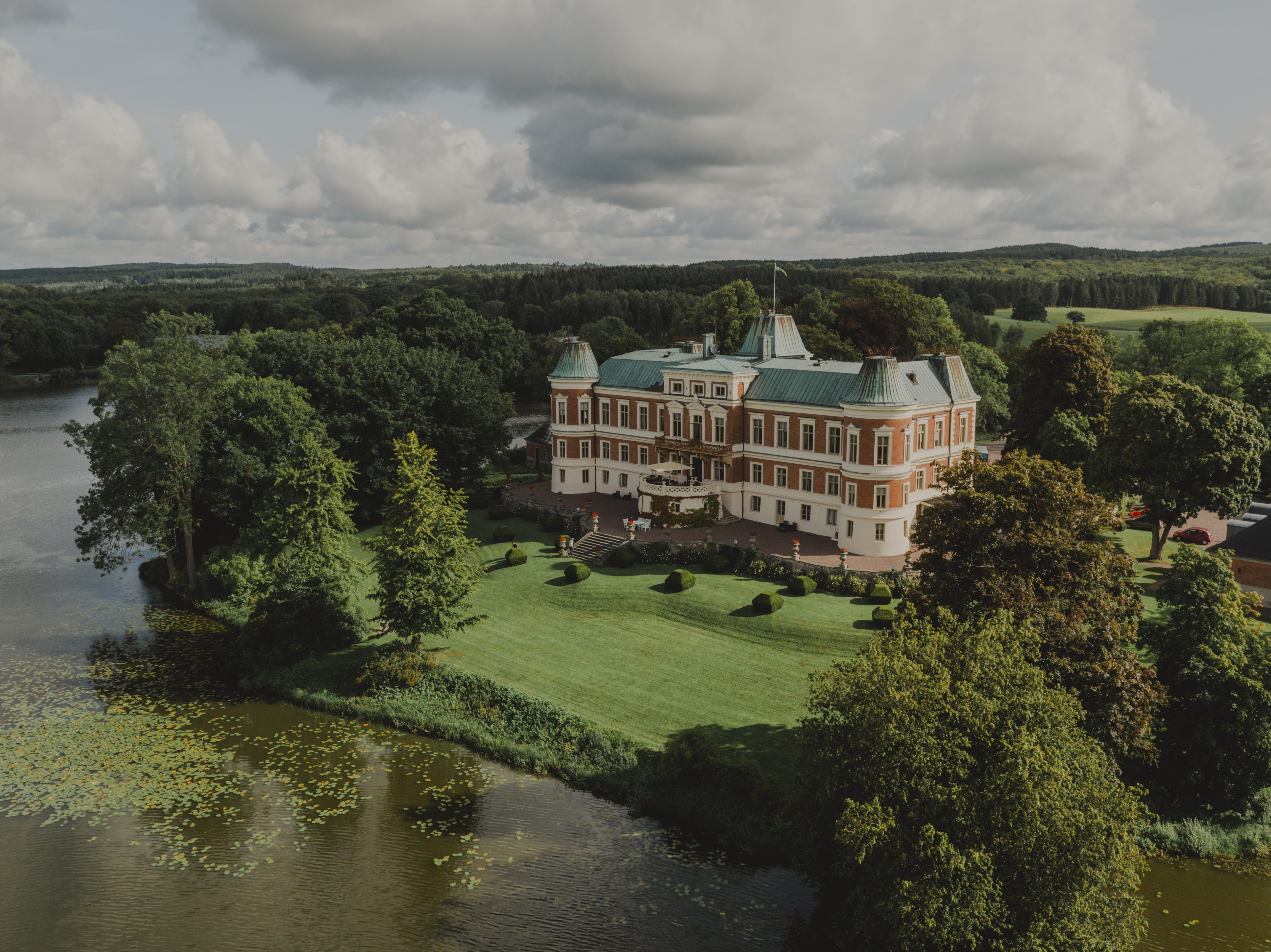 Vue aérienne du château de Häckeberga, un château situé au bord d'un lac, entouré de jardins, de bois et d'une campagne vallonnée en Scanie.