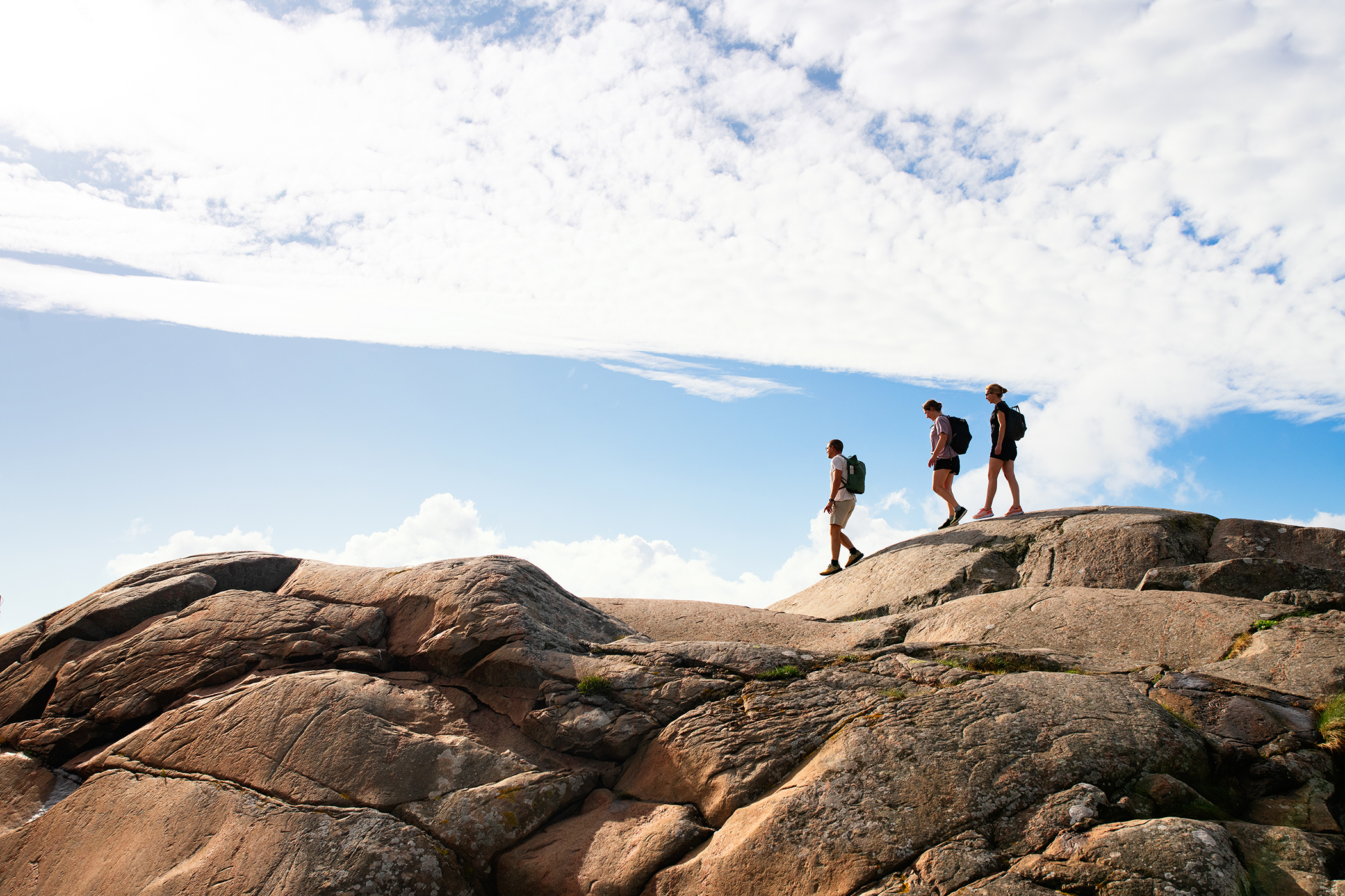 Three people hiking across smooth coastal rocks by the sea near Steninge on Hallandsleden.