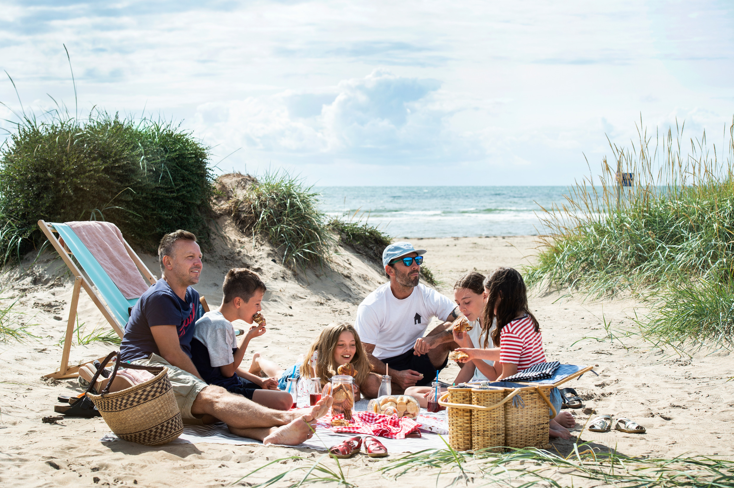 Twee mannen en vier kinderen picknicken op het strand.