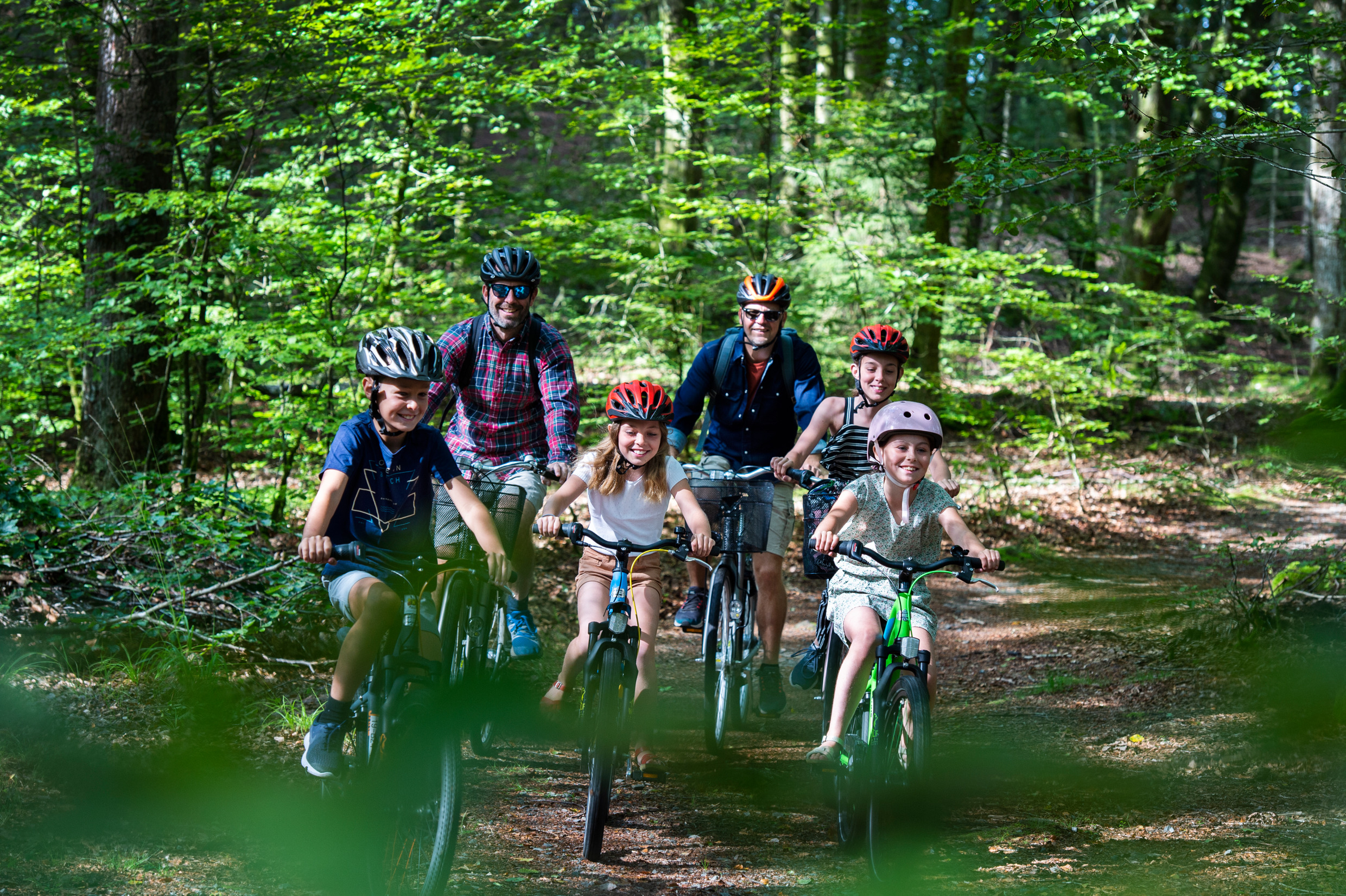 Twee mannen en vier kinderen fietsen in het bos.