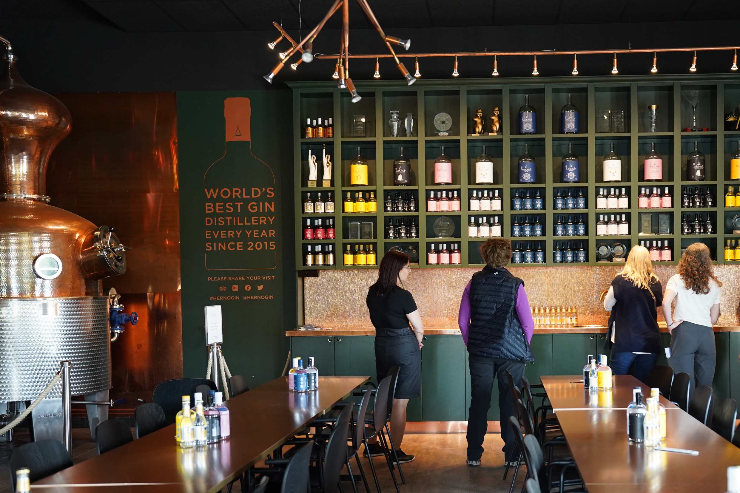 A couple of women stand at a bench to sample gin.
