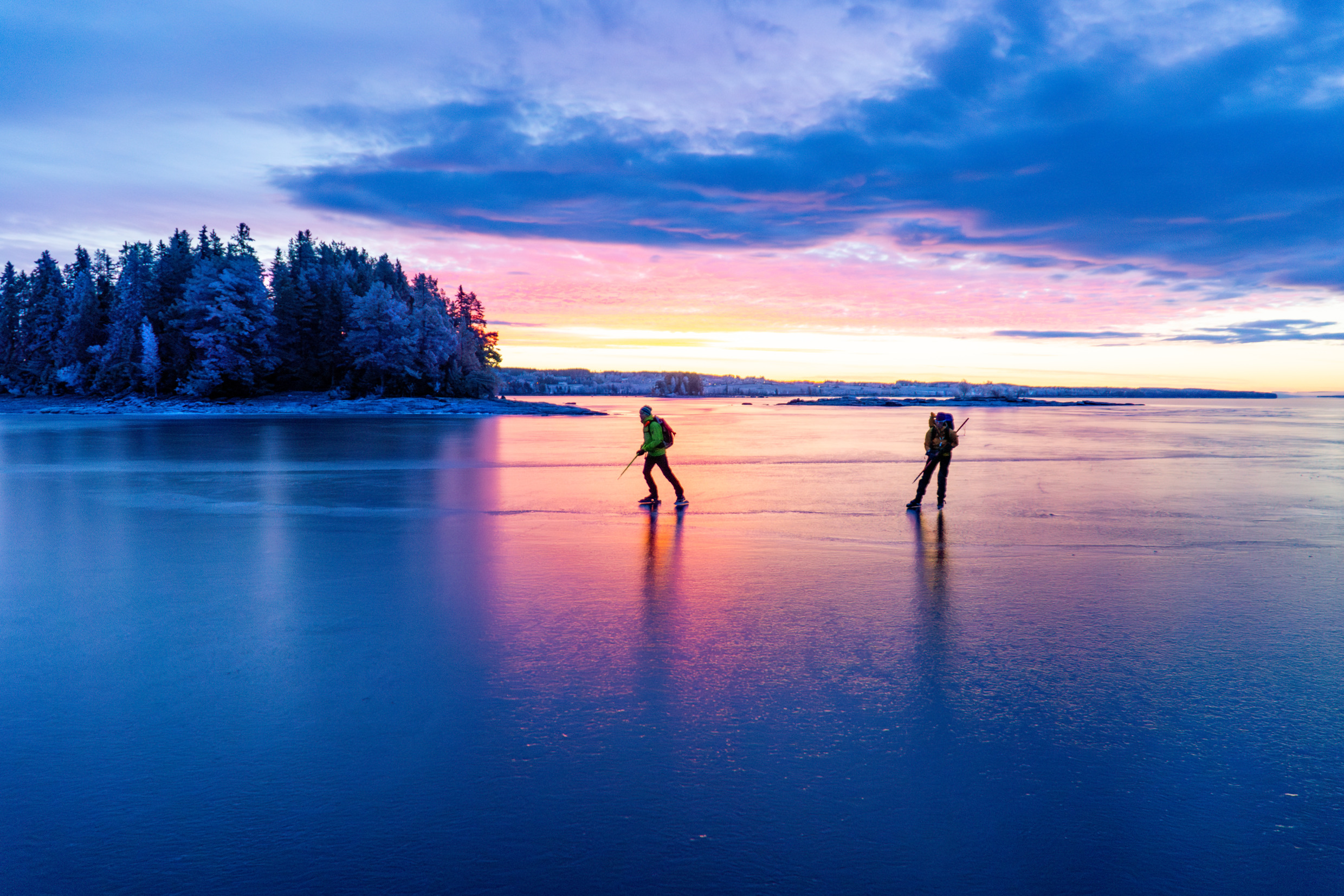 Two people are skating on an ice-covered lake at dusk.