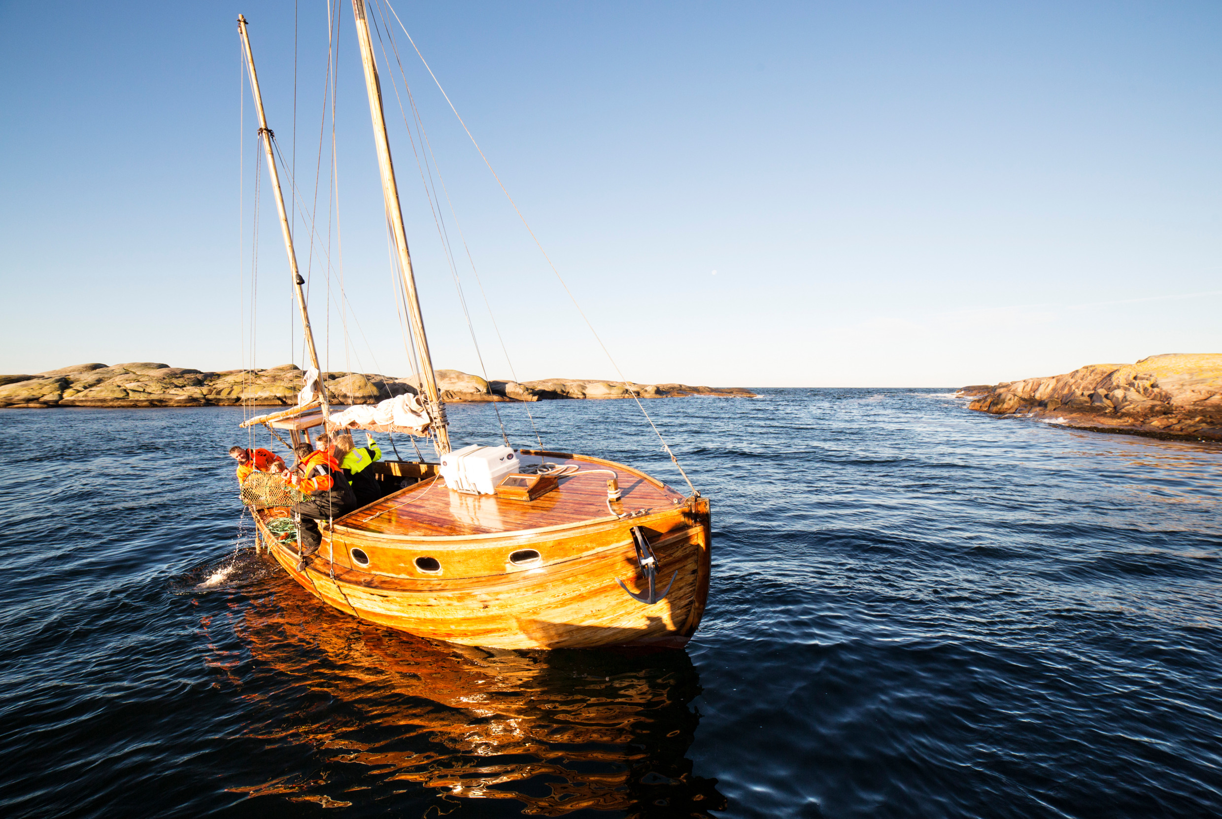 A group of people stand on a fishing boat and watch a person pull up a lobster trap.