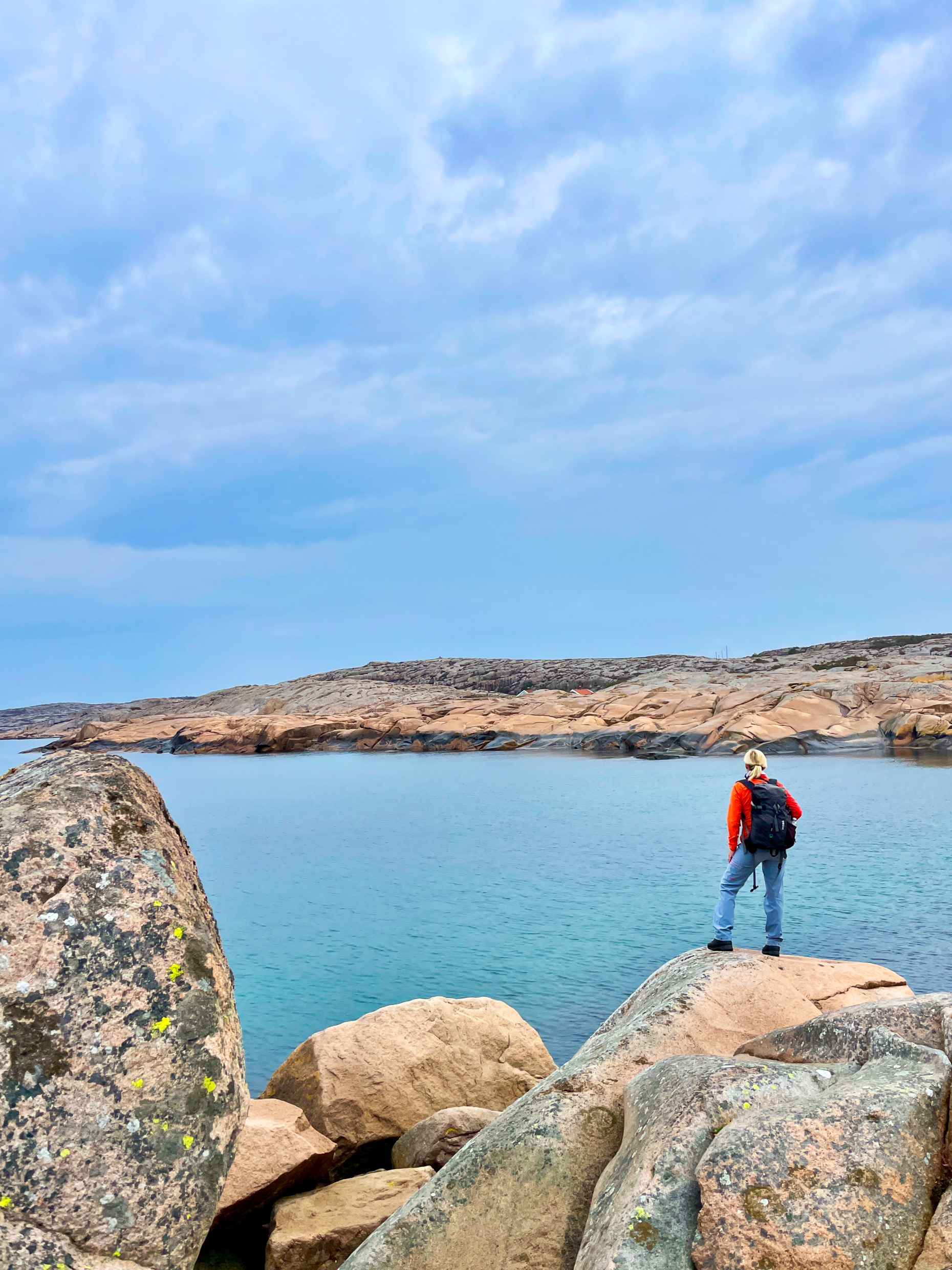 Rocky coastal landscape with pink granite formations, sea views and a distant visitor on the shoreline at Ramsvikslandet in West Sweden.