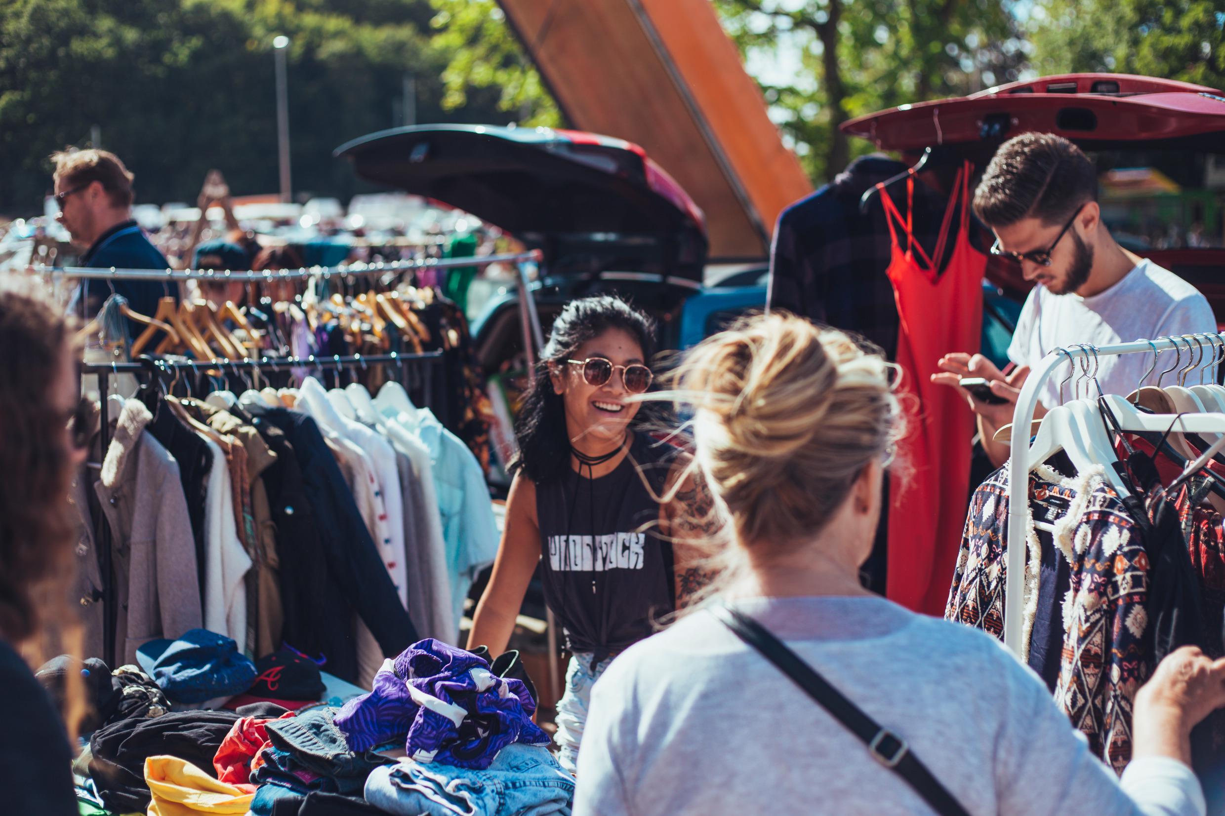 Shoppers bekijken kleding op een vlooienmarkt in de buitenlucht.