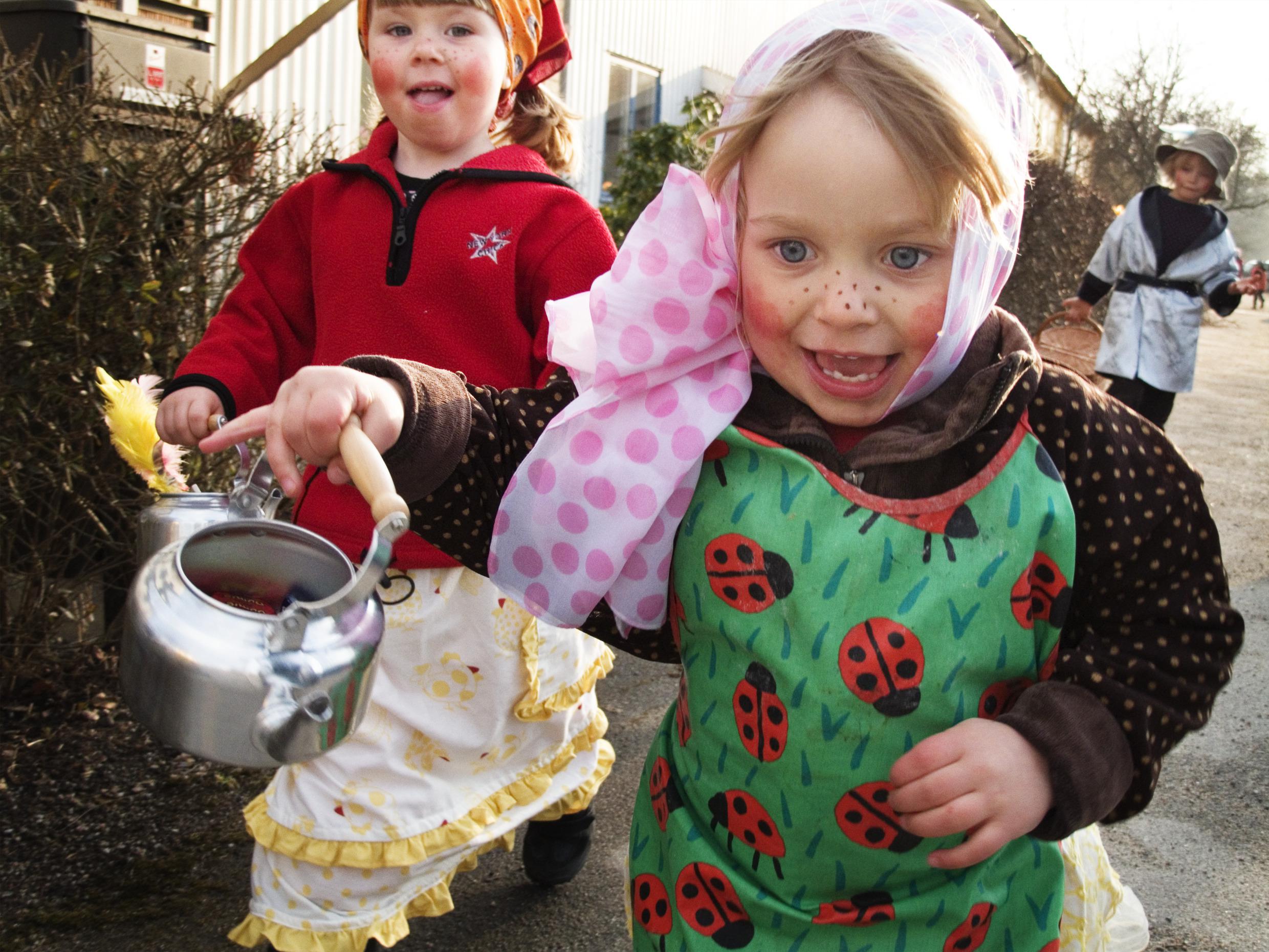 Kinderen rennen over straat met make-up en hoofddoekjes op, verkleed als Paasheksen.