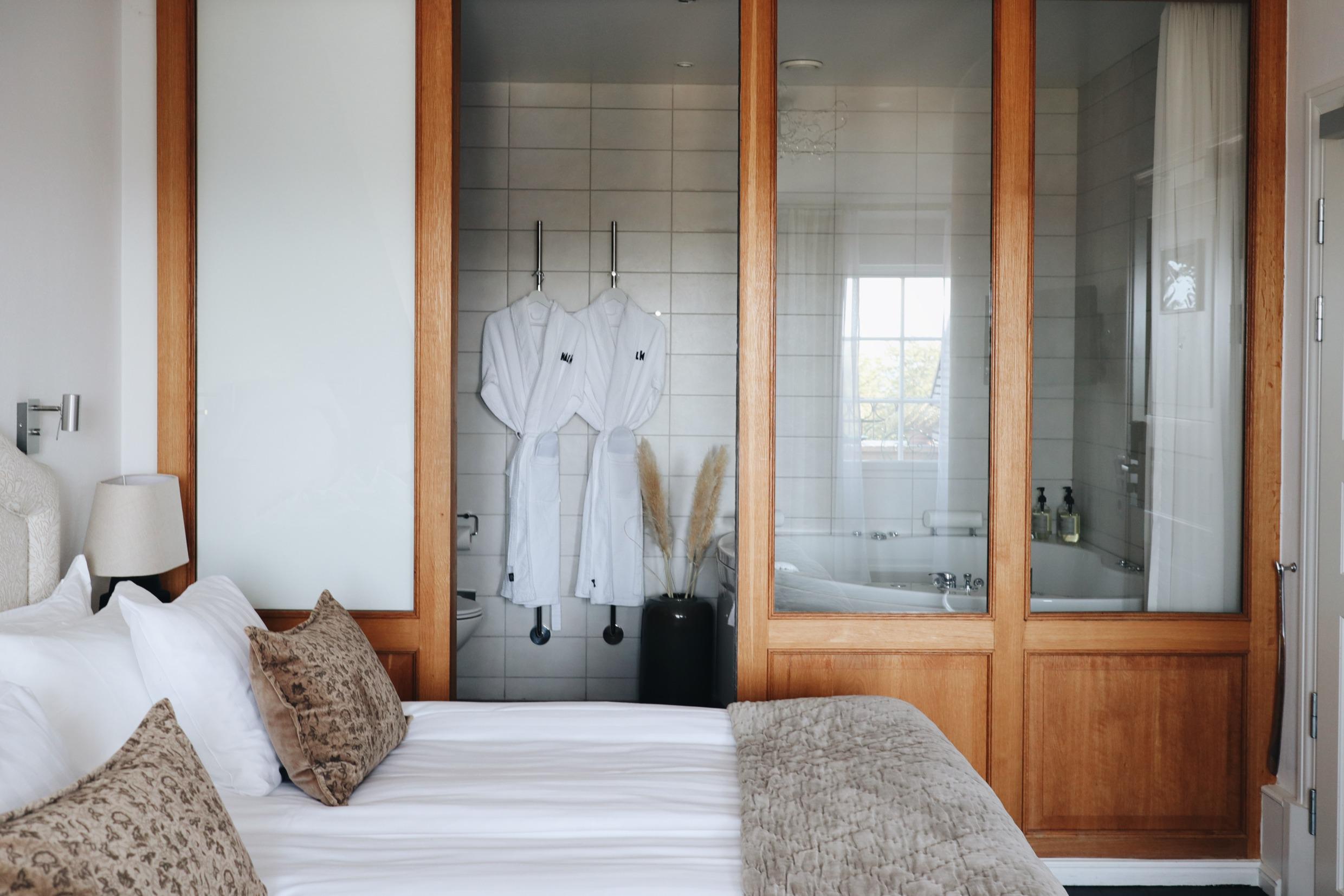 Een hotelkamer met een queensize bed en een badkamer met twee witte badjassen naast een ligbad.