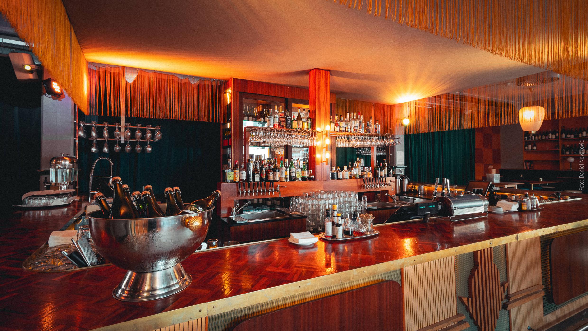 Un bar en bois avec des verres, spiritueux, shakers et autres accessoires.