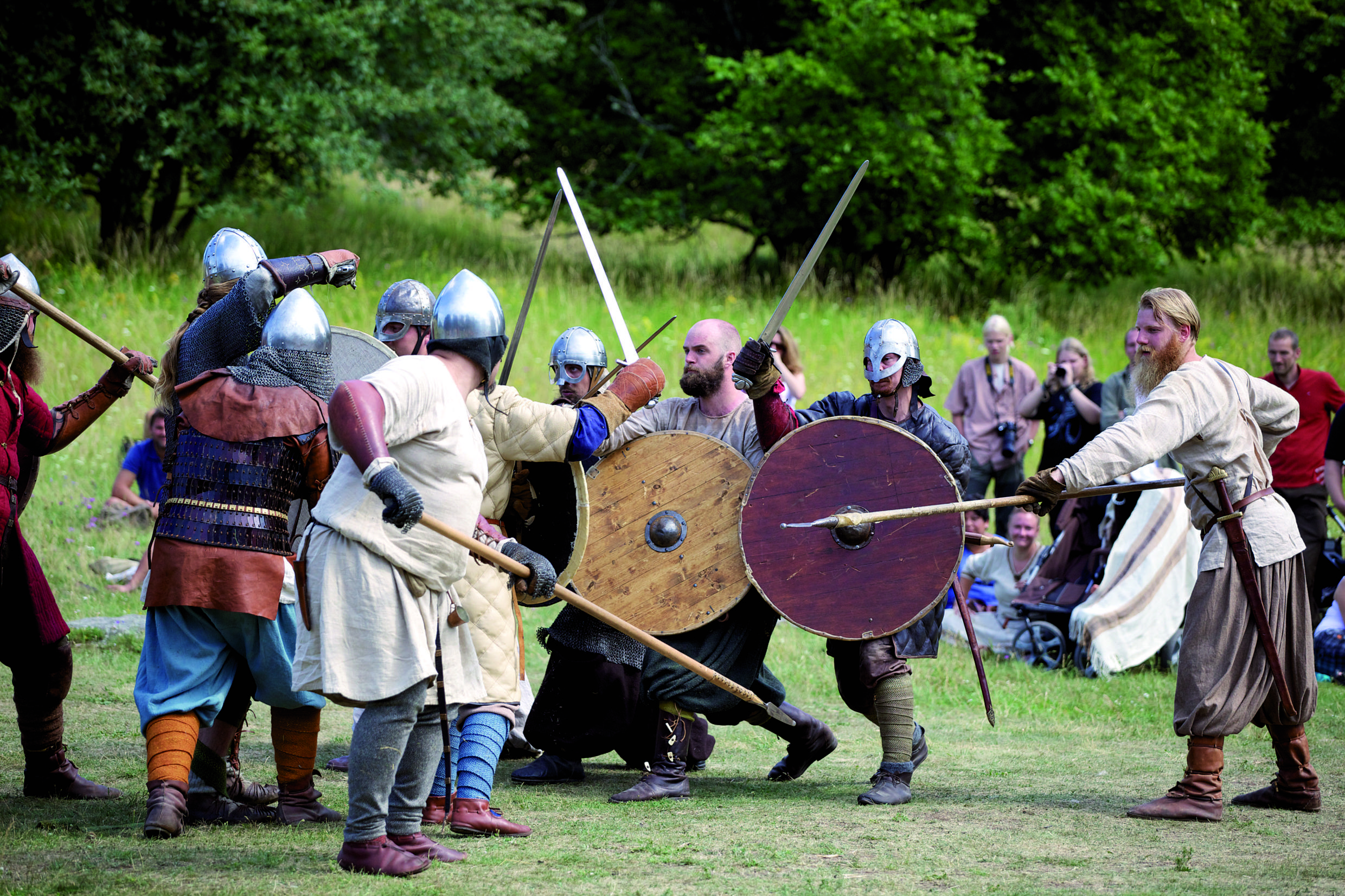 A group of people, all dressed up in viking clothing, is reenacting a battle with spears, swords and shields.