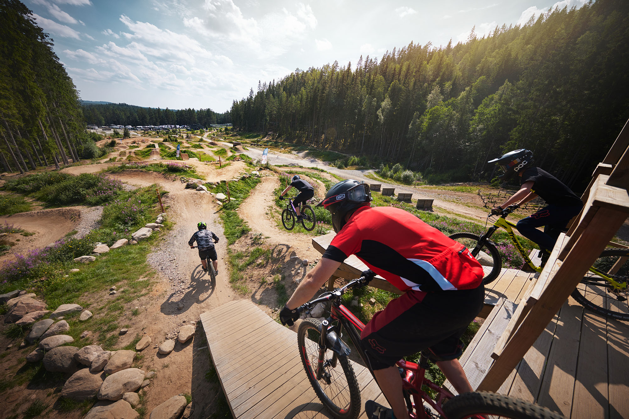 Group of cyclists riding downhill on a dirt trail with curves, bumps and ramps at Isaberg Mountain Resort’s MTB Bike Park, surrounded by forest.