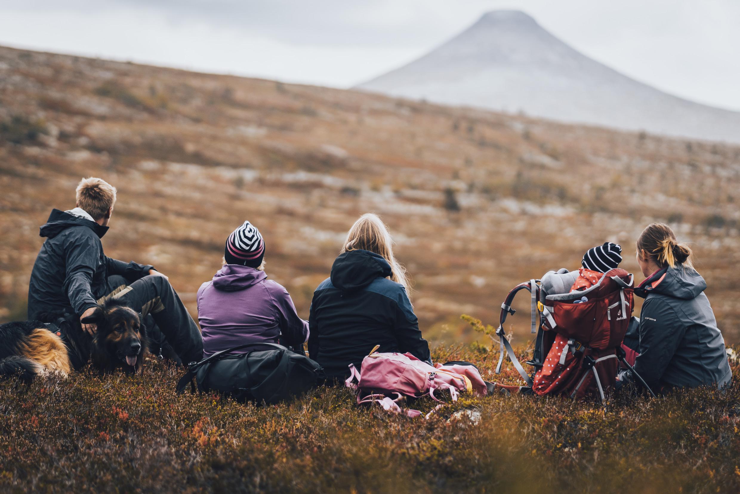 Five people and a dog sitting in on the ground in the mountain area of Idre.