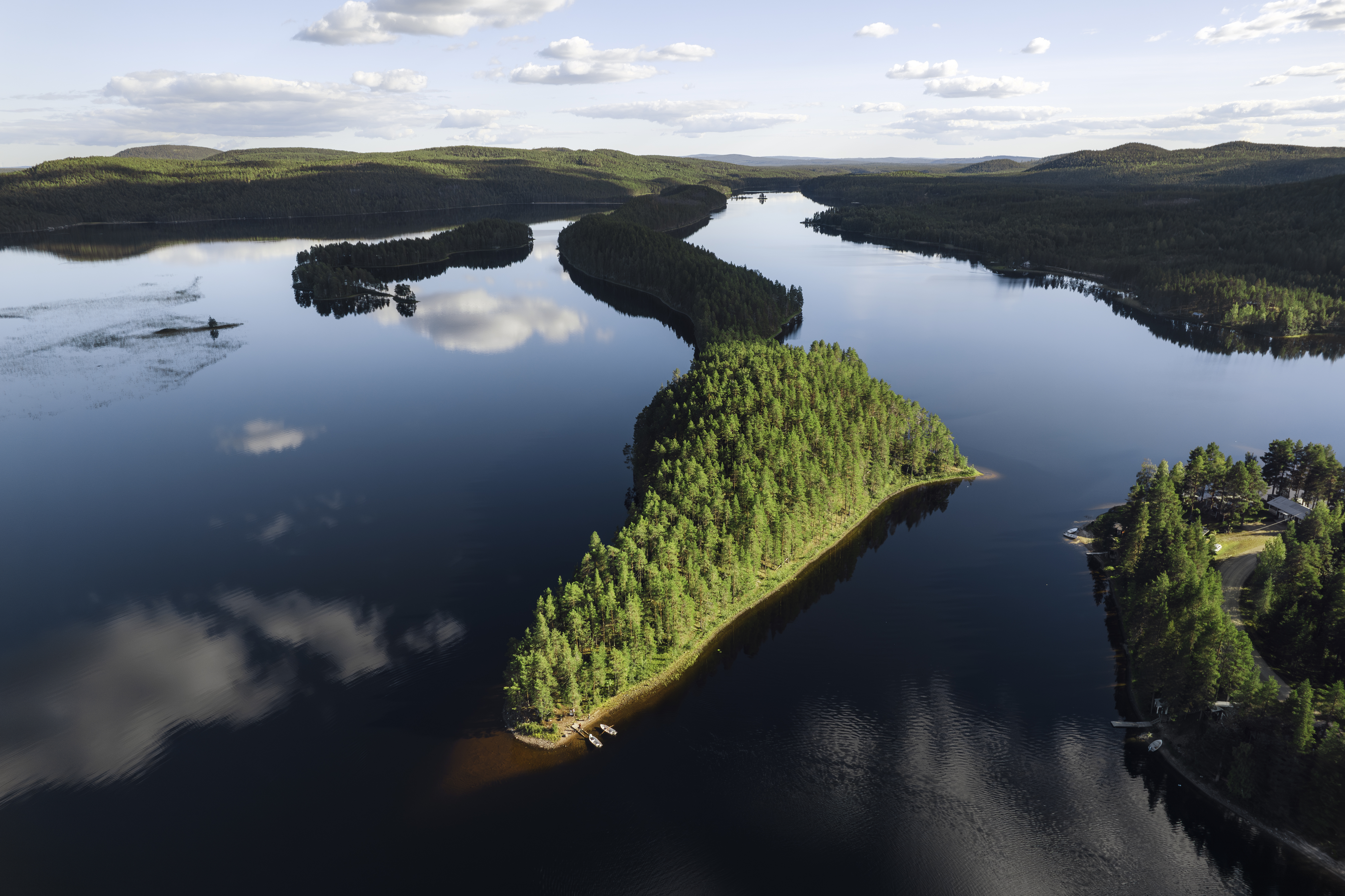 Aerial view of a narrow, forest-covered peninsula surrounded by calm water, illustrating the landscape along the Isälvsleden trail in Västerbotten.