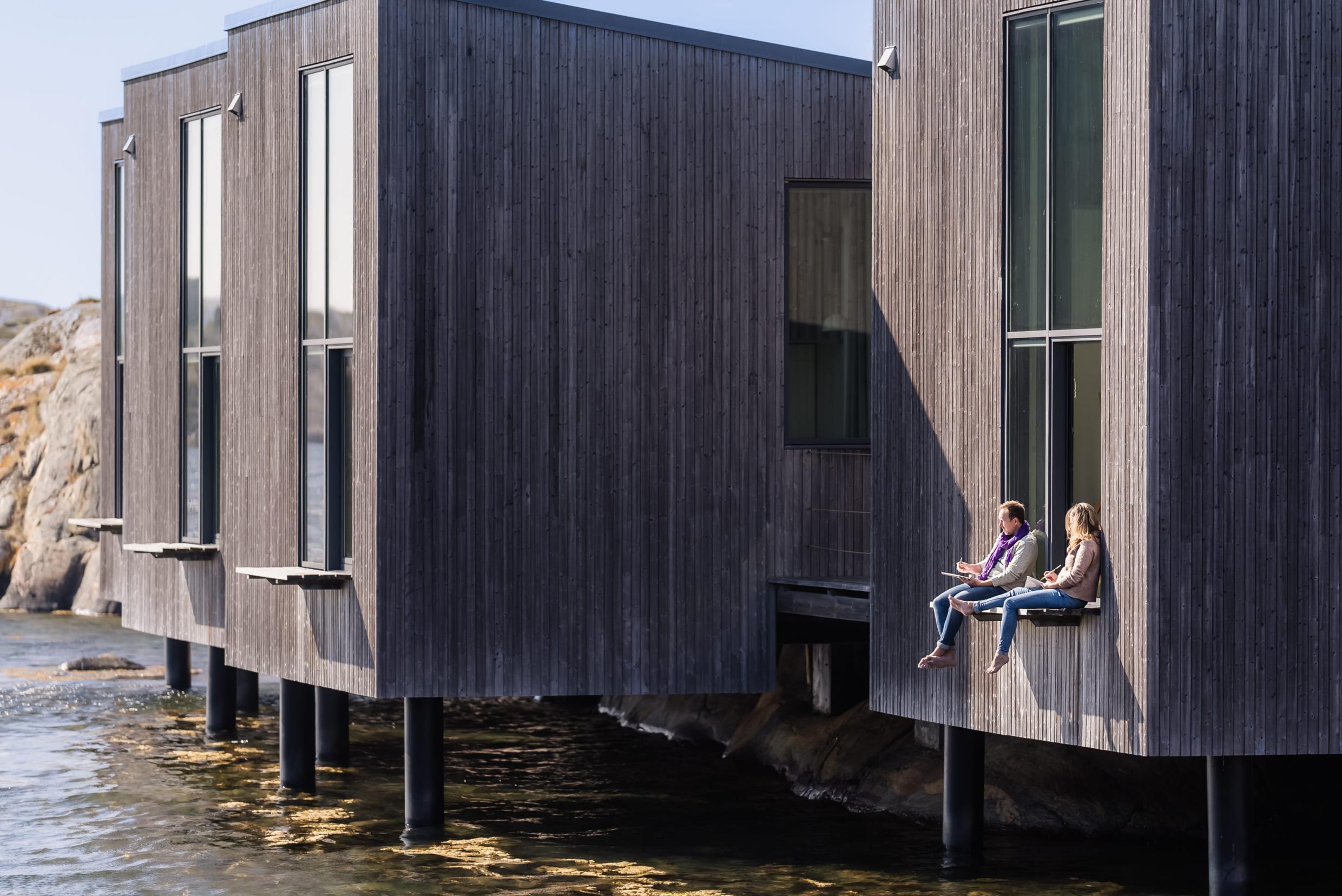 Een man en een vrouw zitten op een balkon met uitzicht op het water terwijl ze schilderen.