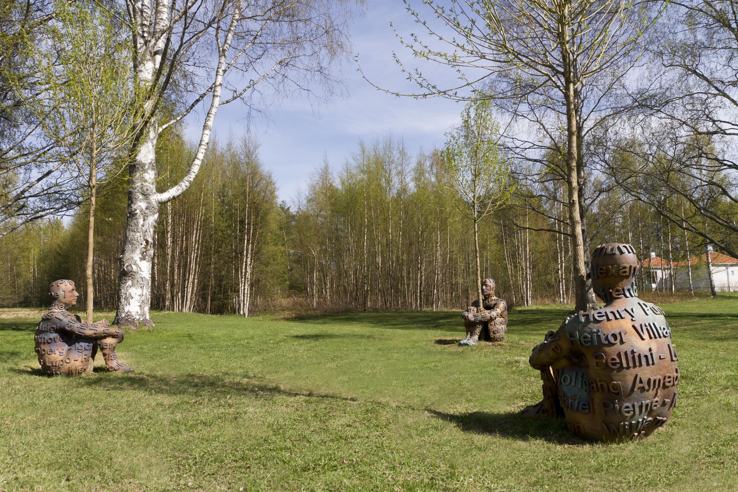 Three sculptures shaped like humans sitting down hugging a tree each at Umedalen Sculpture Park.