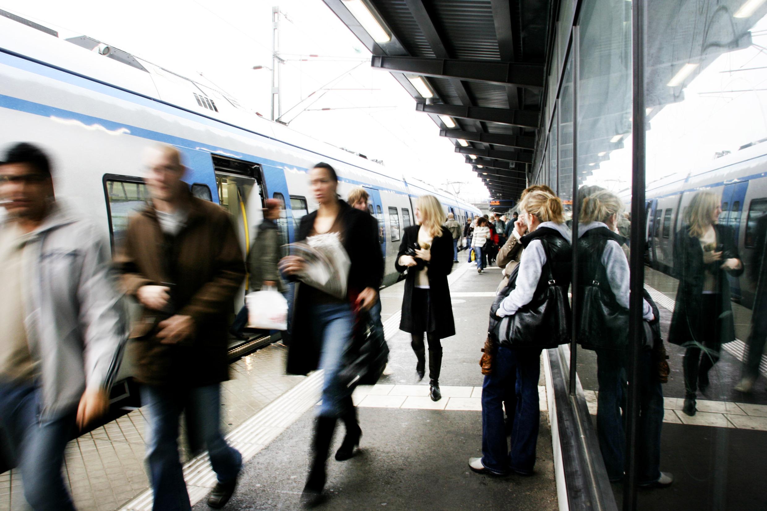 People are seen entering and exiting a subway (metro) train at a busy above-ground subway station.