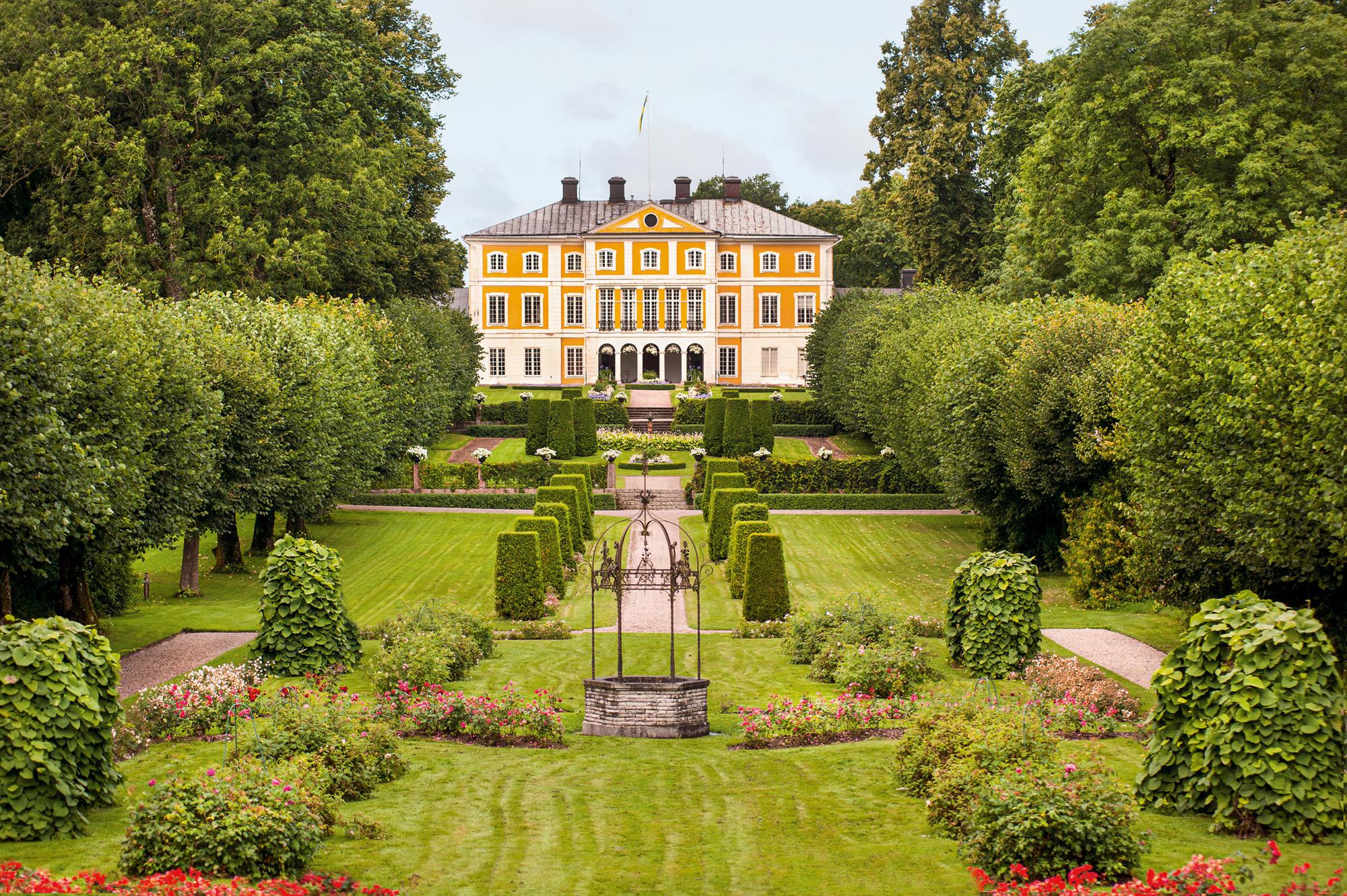 Un jardin luxuriant devant la façade jaune du manoir Julita.