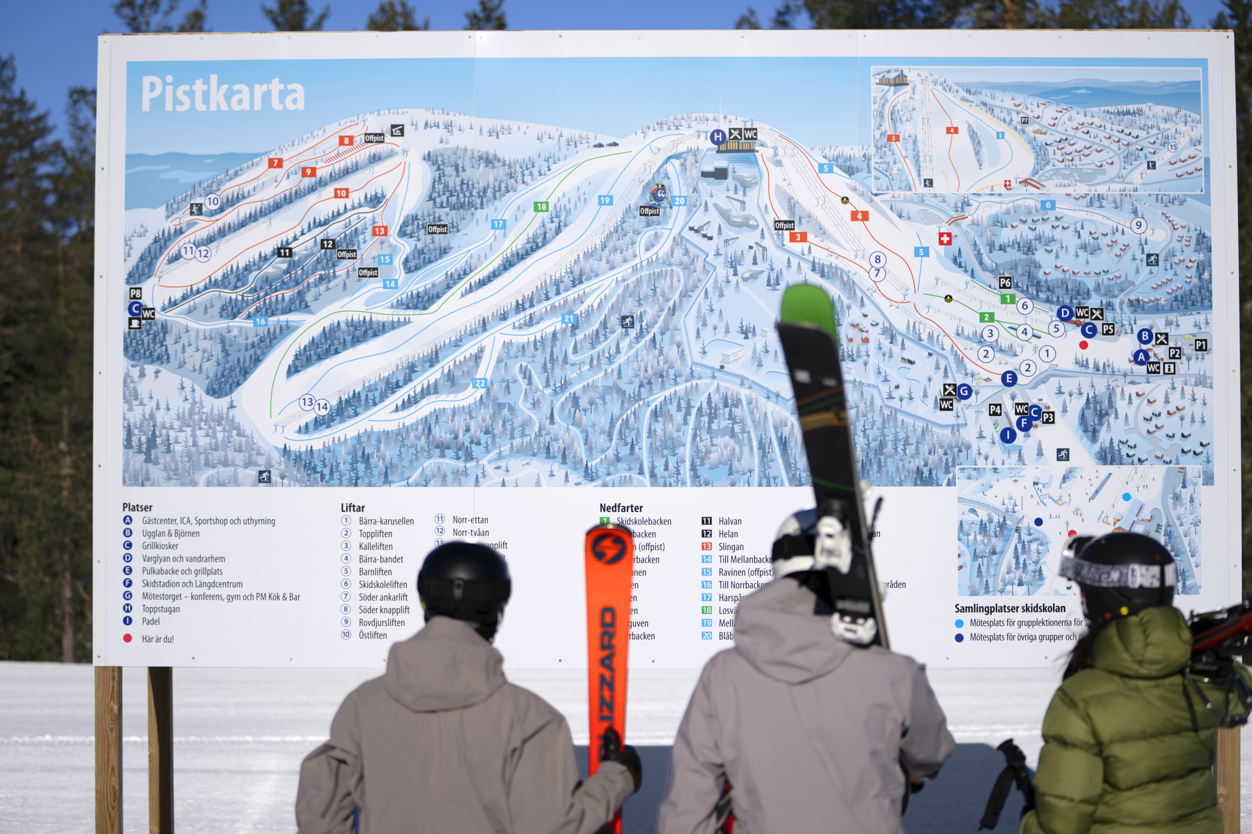 Drei Personen mit Skiern betrachten einen Pistenplan in Grönklitt