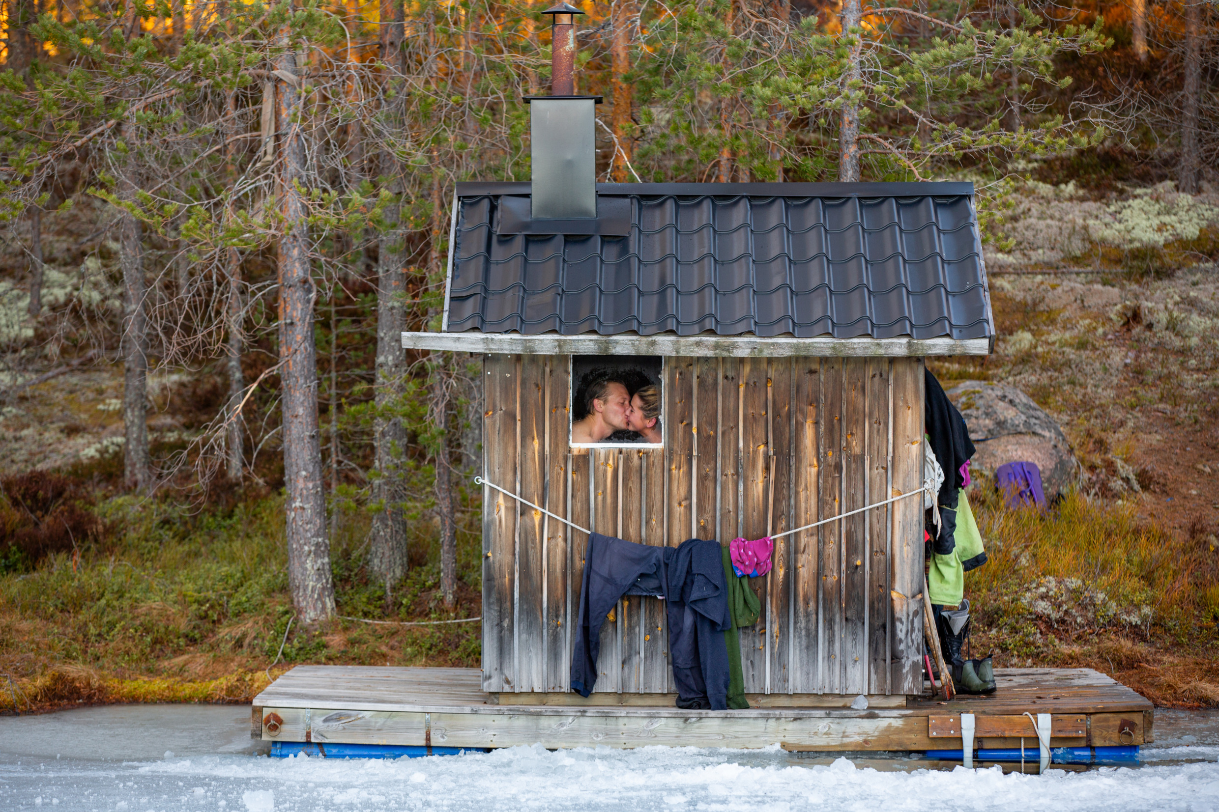 Eine Sauna am Wasser. Im Fenster sieht man ein küssendes Paar.