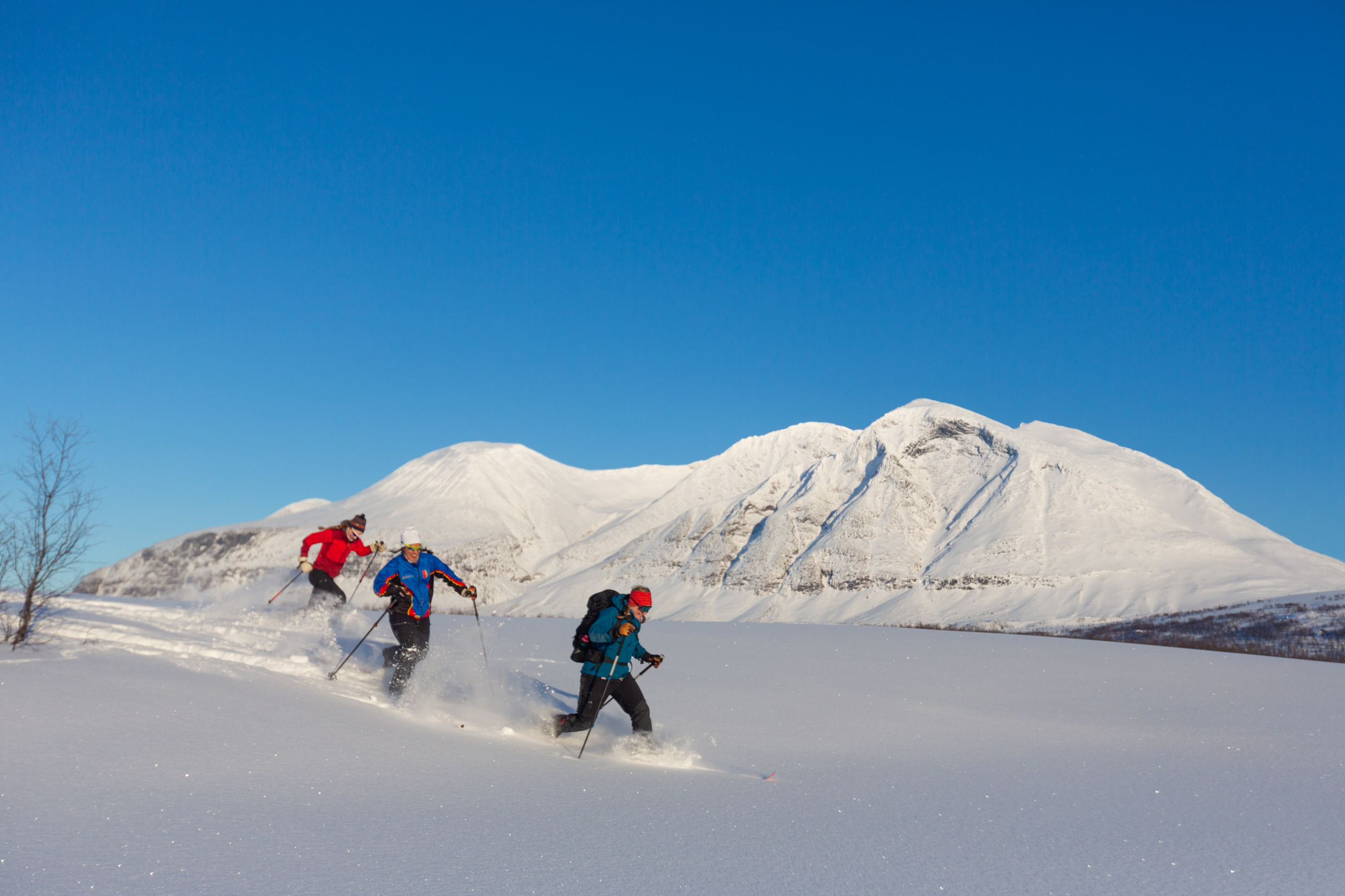 Trois personnes font du ski de fond dans un paysage hivernal par une journée ensoleillée.