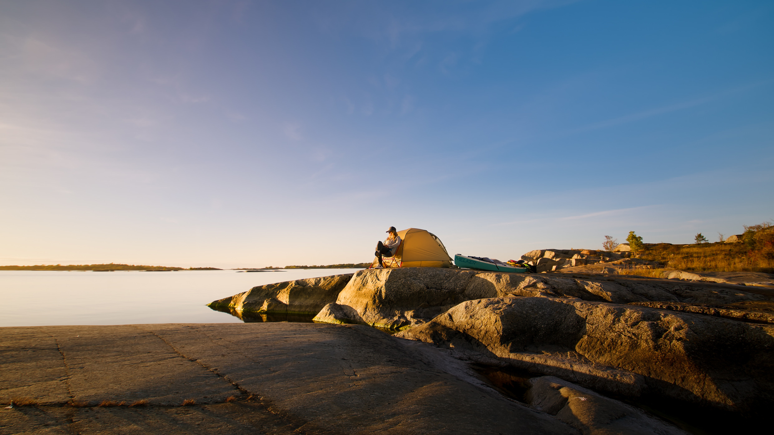 A woman sits next to a yellow tent by the water on an island in the archipelago.